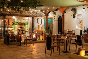 Un espacio exterior para comer con mesas y sillas, una chimenea y plantas colgantes.