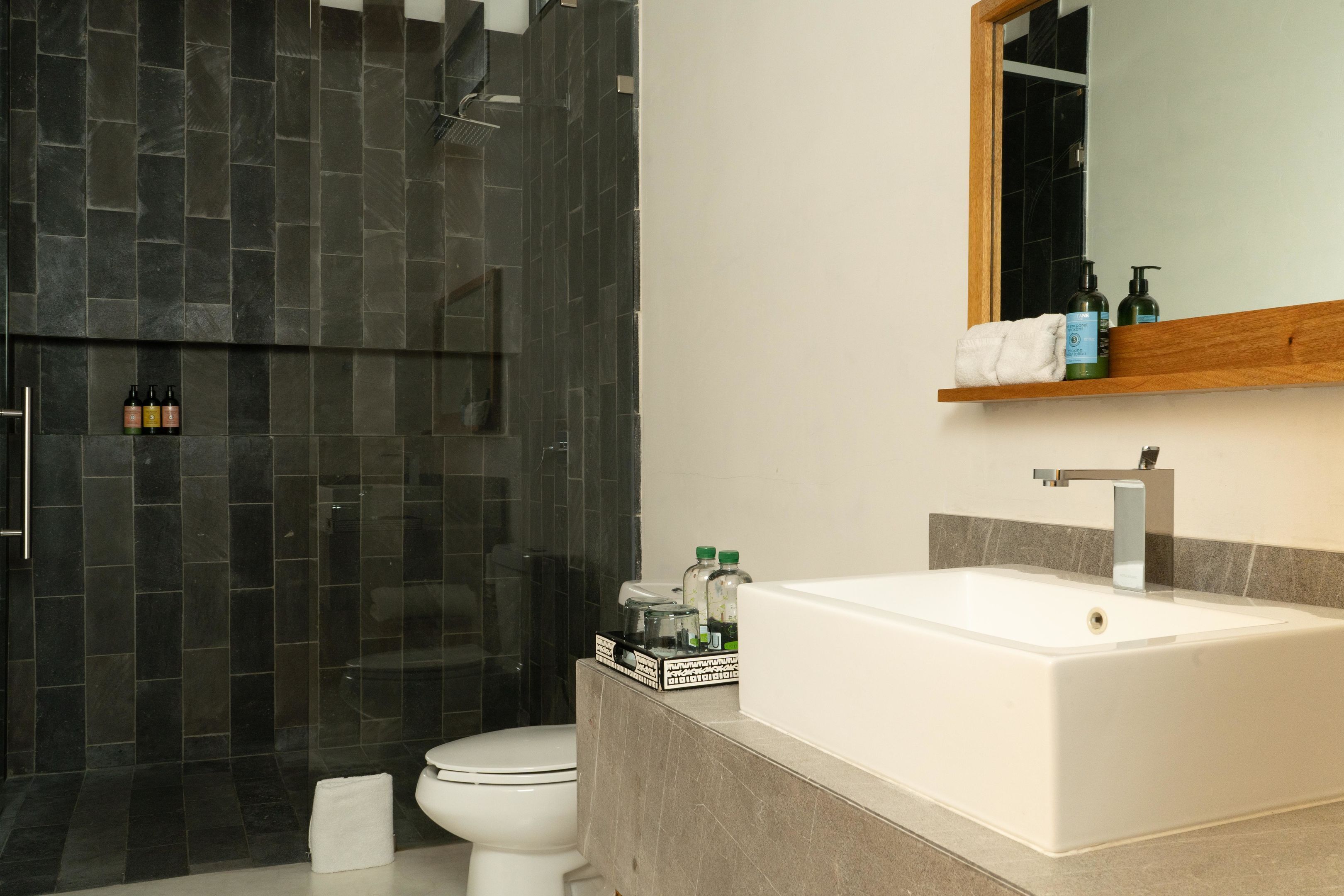 Une salle de bain moderne avec une grande baignoire blanche, une douche en verre et une étagère en bois au-dessus du lavabo où sont rangés les articles de toilette.