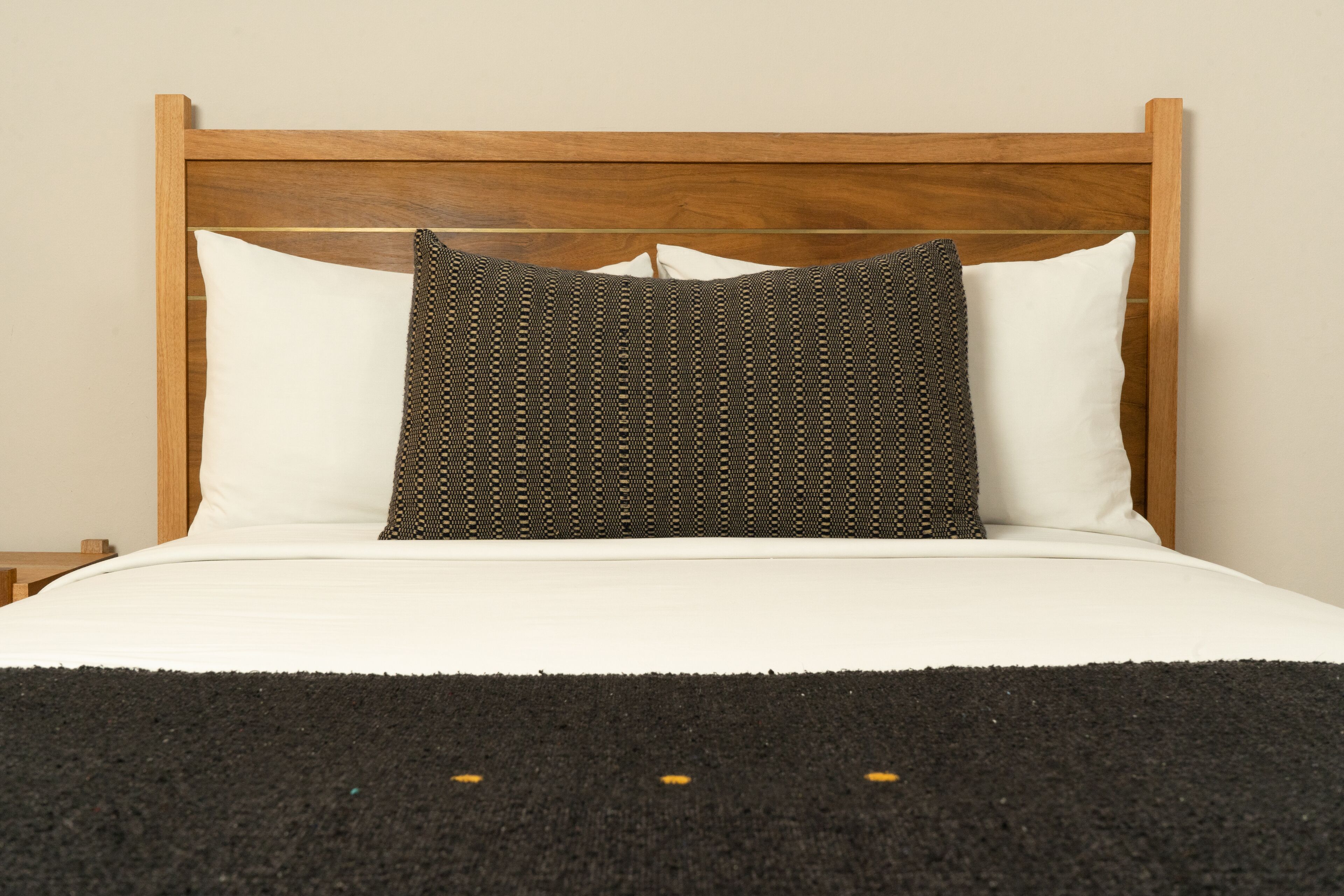 A bed with a wooden headboard, white pillows, and a dark patterned pillow.