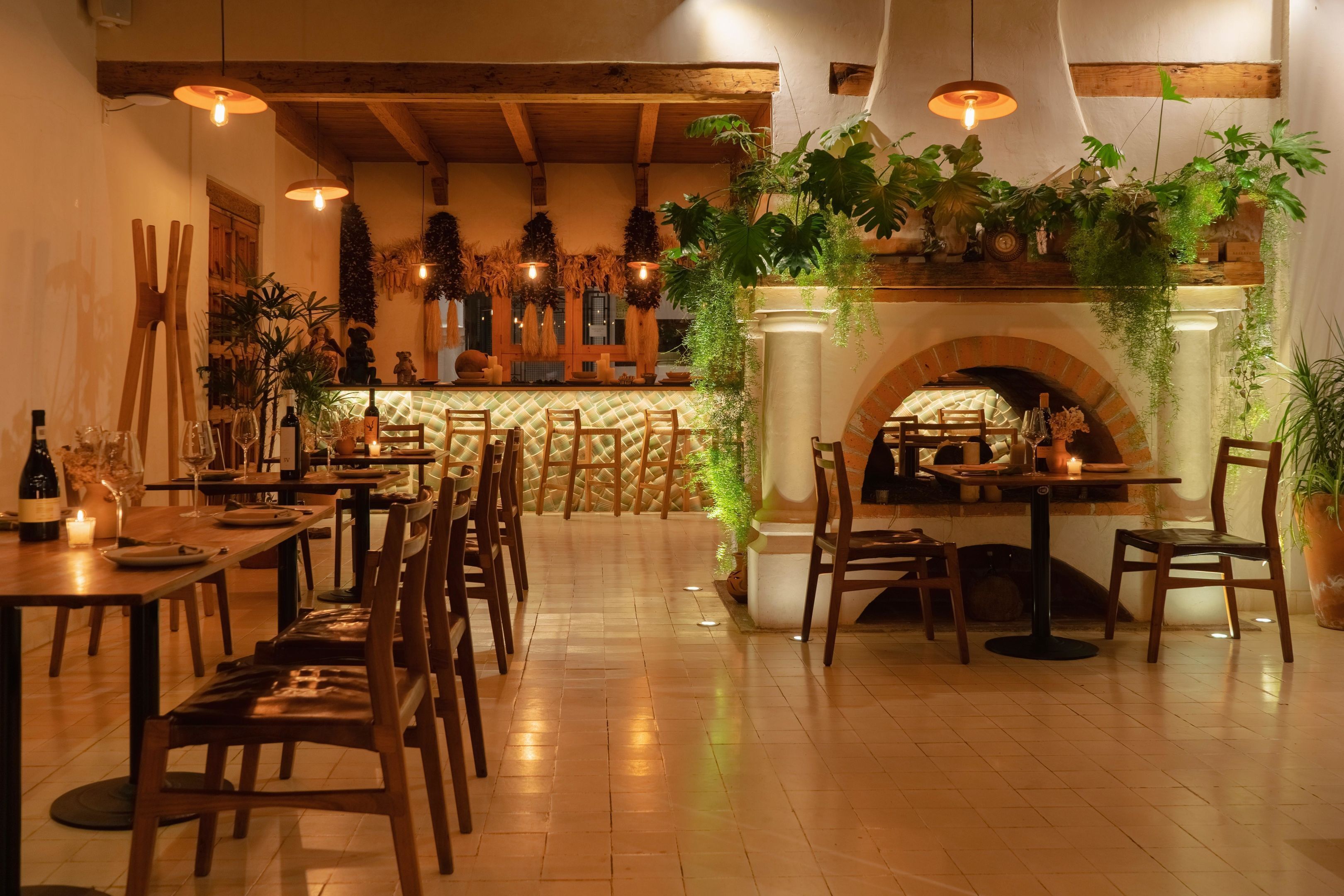 Un restaurante con mesas y sillas de madera, una chimenea de ladrillo y plantas colgantes.