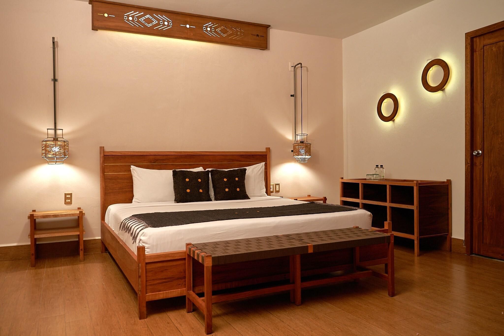 A neatly arranged bedroom with a wooden bed, bedside tables, a bench, and wall-mounted lighting fixtures.