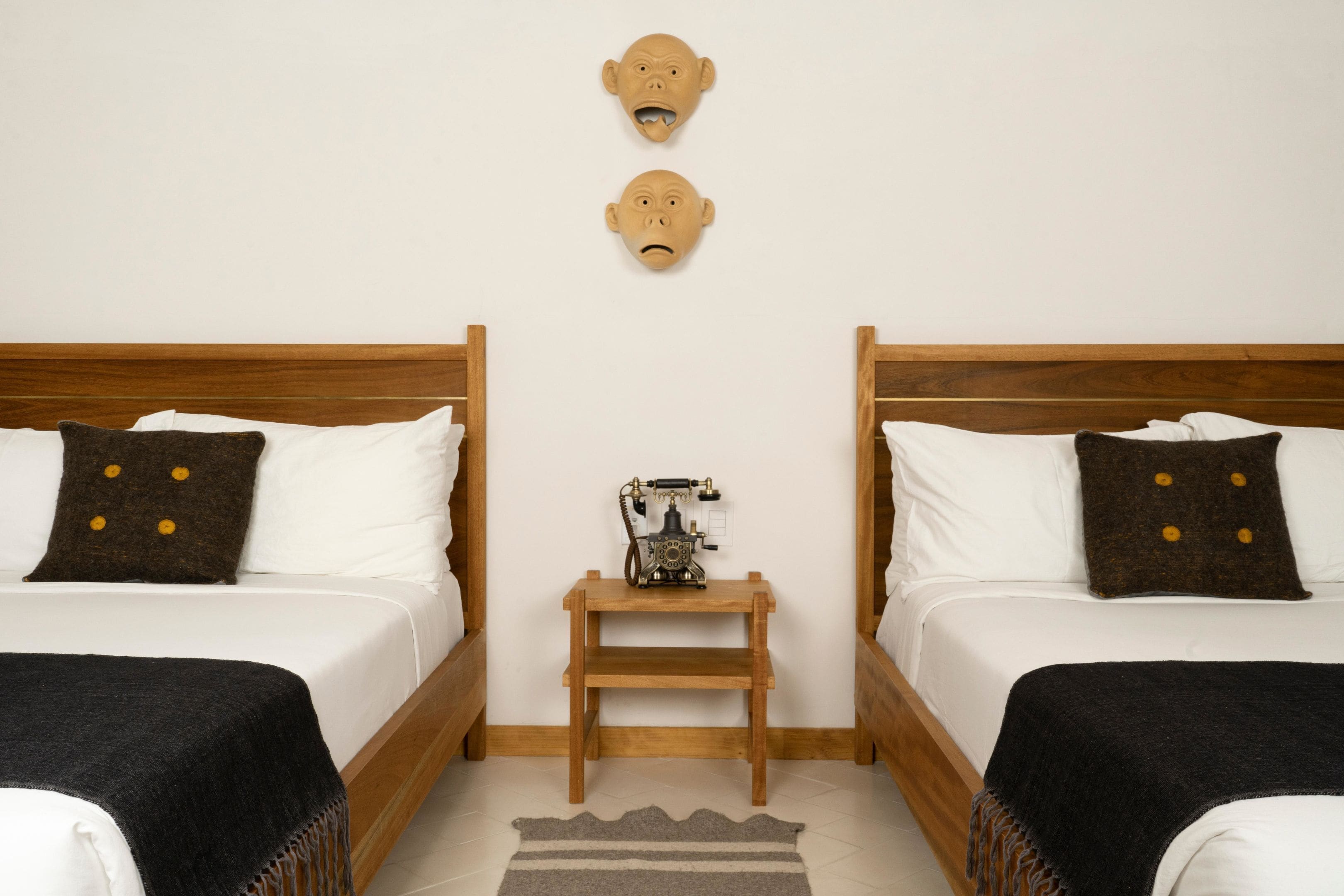 A hotel room with two beds, a wooden nightstand, and a wall-mounted telephone.