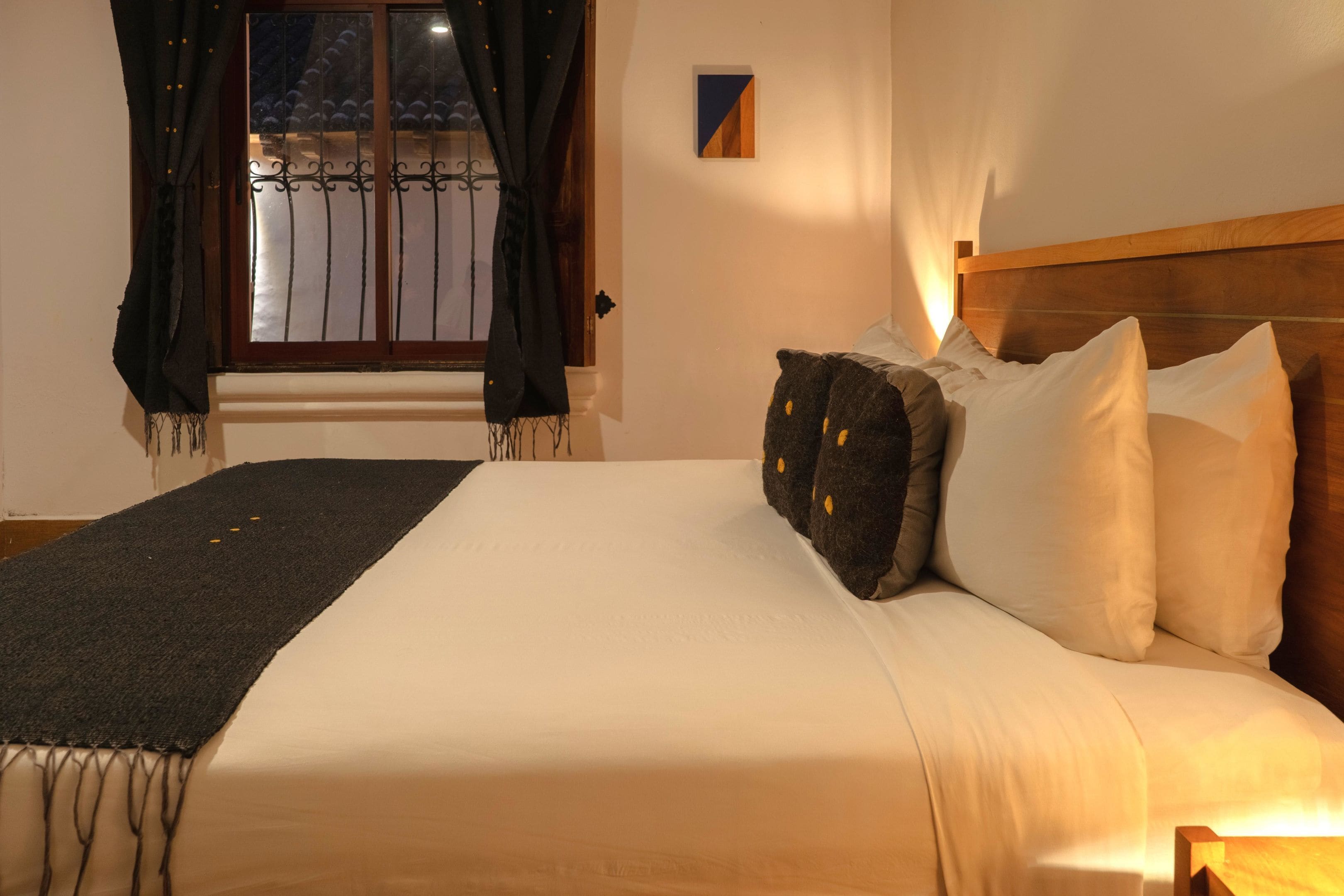 Un lit bien fait, avec des oreillers blancs et foncés, une tête de lit en bois et un plaid noir.