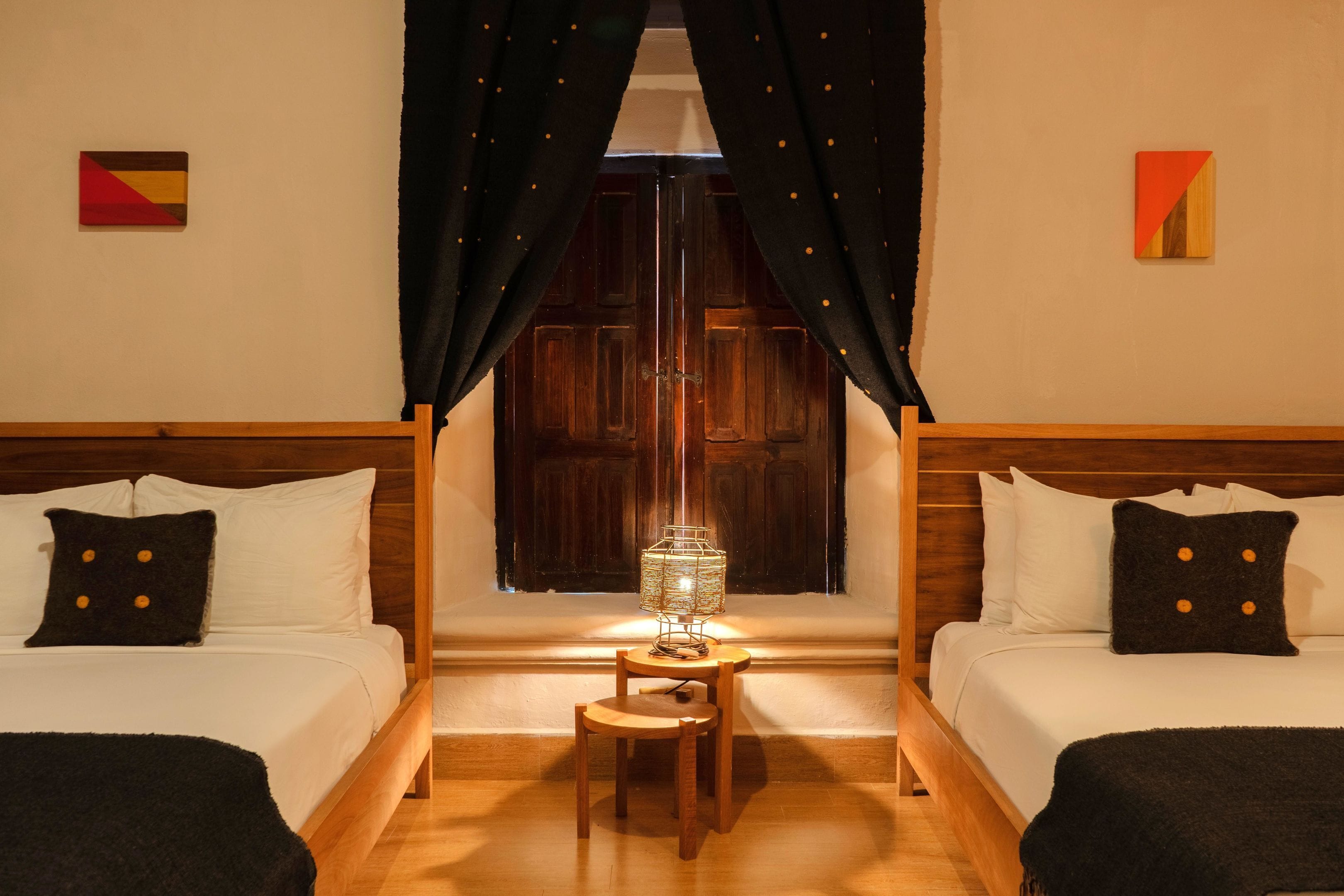 Una habitación con dos camas, una mesita con lámpara y una ventana con cortinas.