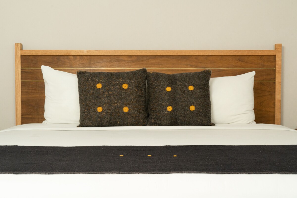 A bed with a wooden headboard, two white pillows, and two dark pillows with yellow buttons.