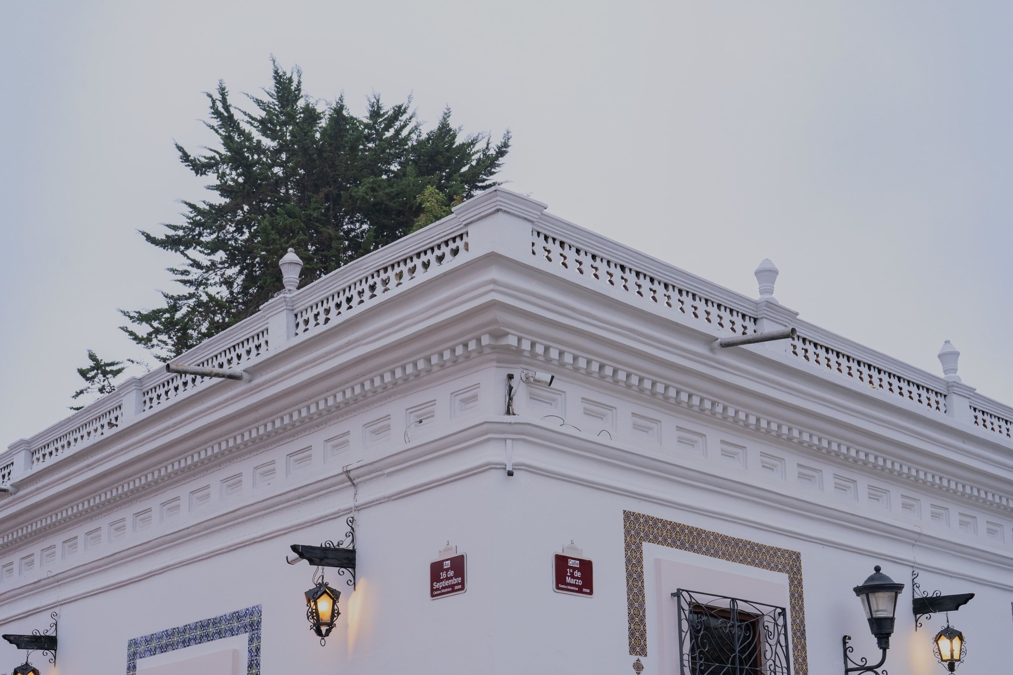 Un edificio blanco con molduras decorativas y un balcón. Dos letreros indican el nombre y la fecha del edificio.