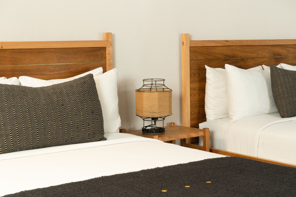 A double bed with white and patterned pillows, a small wooden nightstand with a lamp, and a black rug.