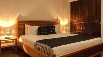 A wooden bed with white bedding and a dark throw blanket, flanked by two bedside tables with lamps.