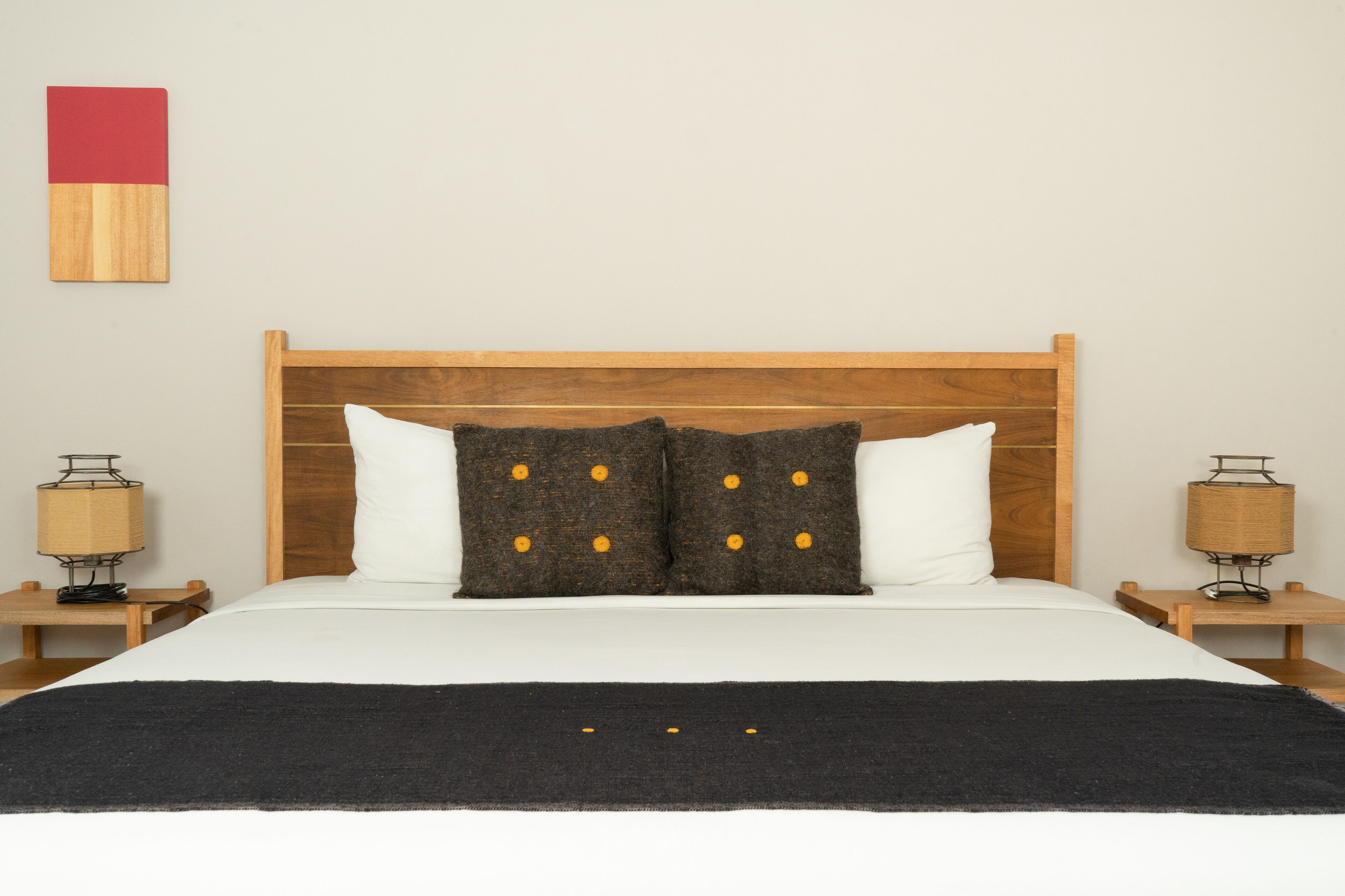 A neatly made bed with a wooden headboard, two bedside lamps, and a black throw blanket.