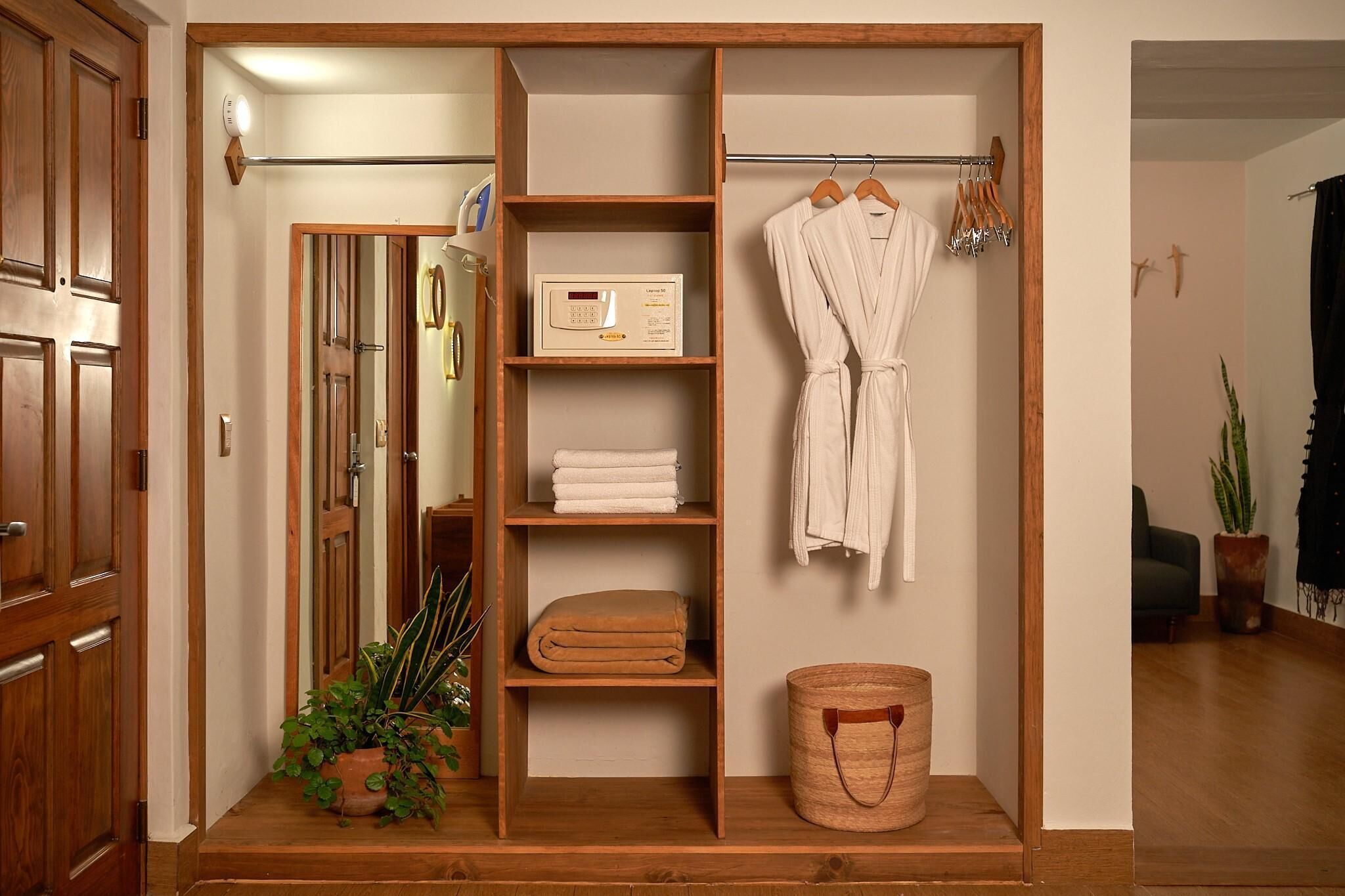 A wooden wardrobe with shelves for folded clothes, a hanging robe, and a small basket.