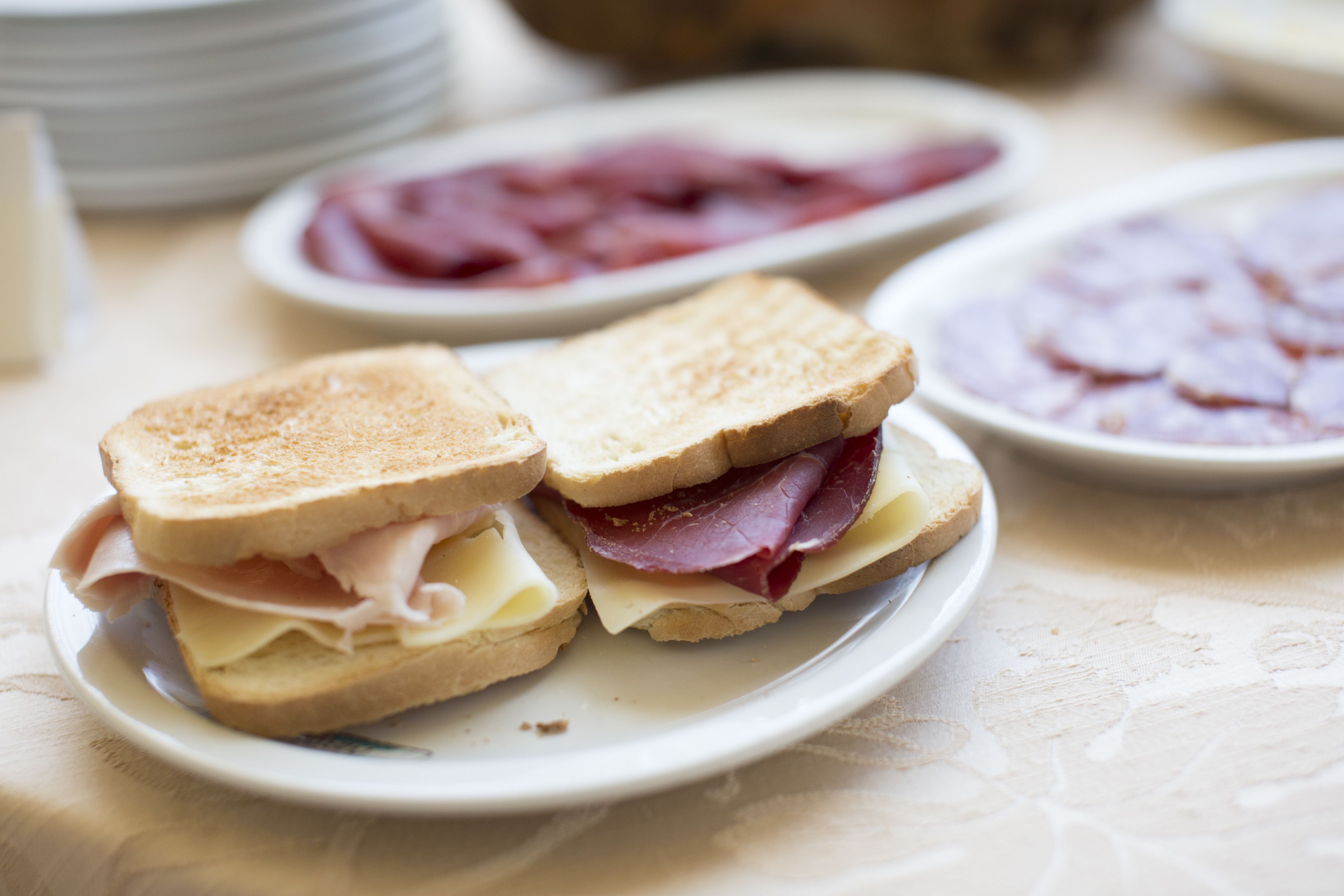 A sandwich on a plate with ham and cheese, surrounded by other food items on a table.