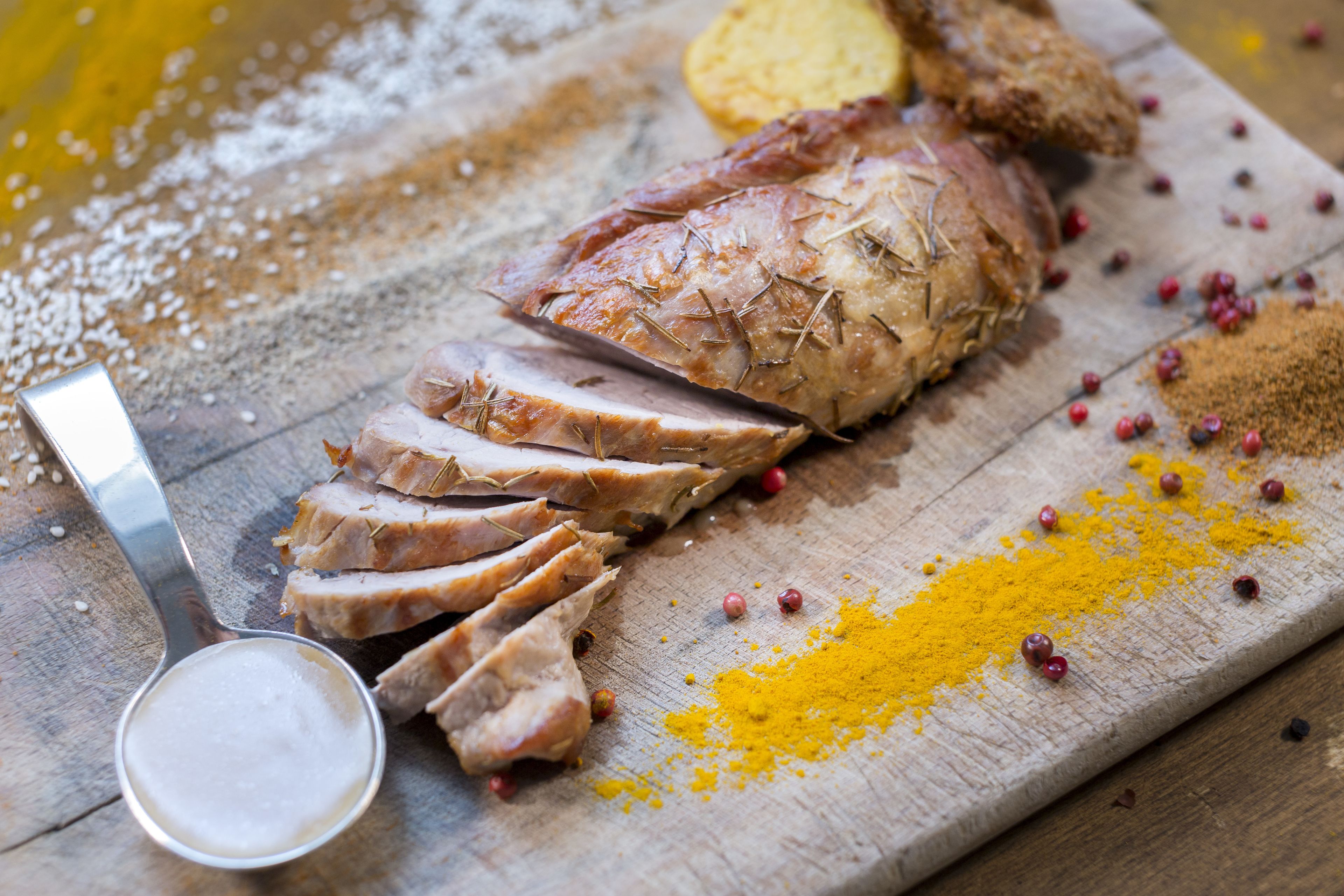 A wooden cutting board with sliced meat, spices, and a measuring spoon.