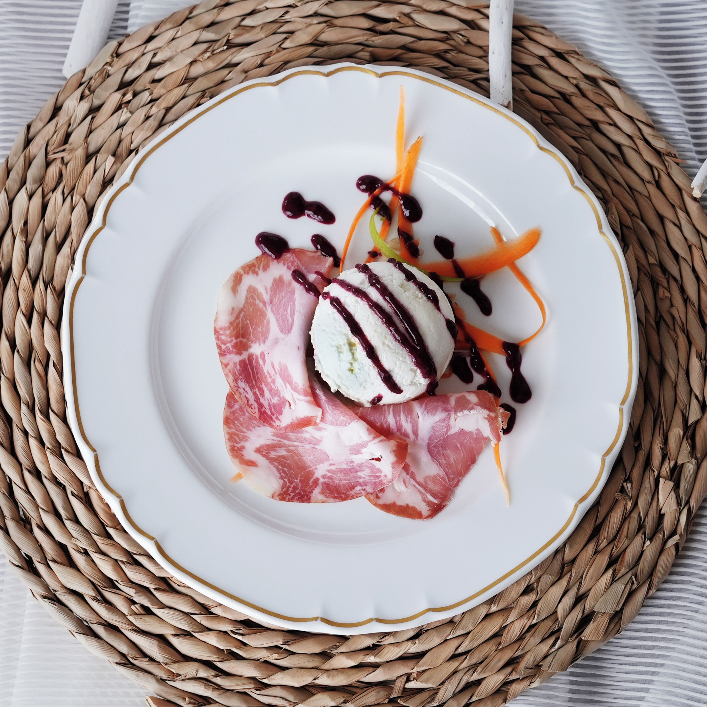 Ein weißer Teller mit Fleisch, einer Kugel Eis und Gemüse auf einer gewobenen Unterlage.