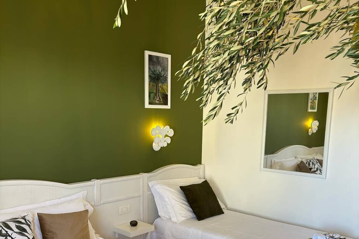 A hotel room with two beds, a green wall, a framed picture, and a mirror.