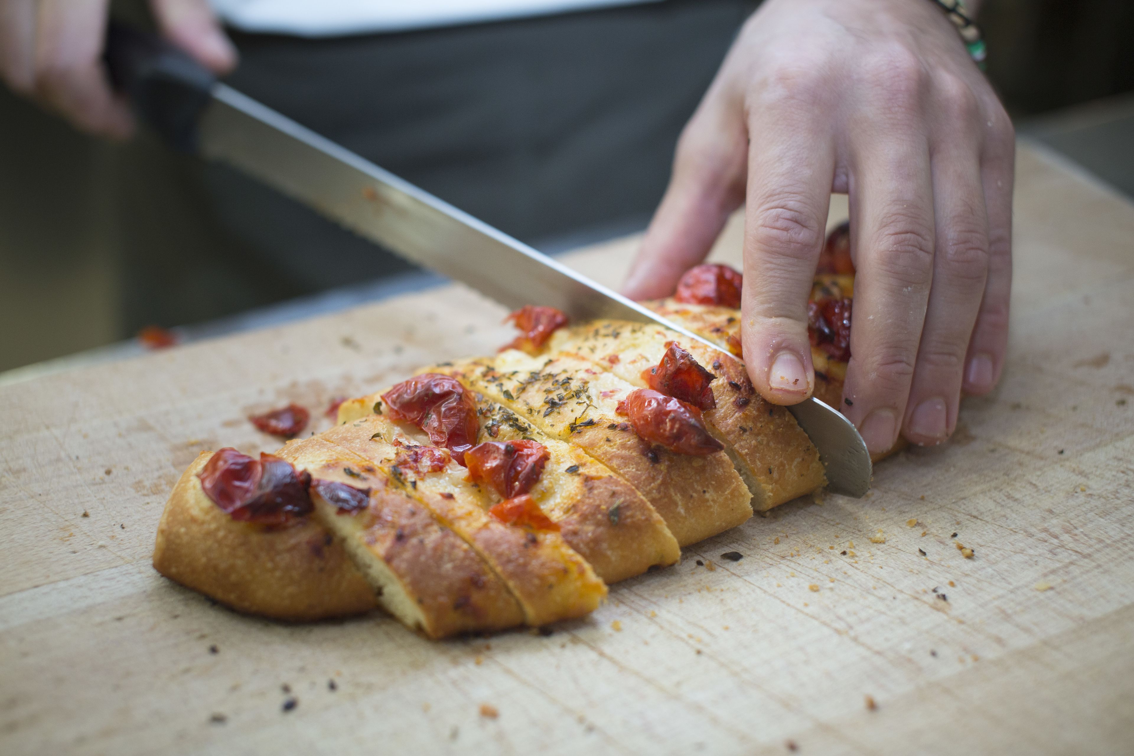 A person slicing a pizza on a wooden cutting board.