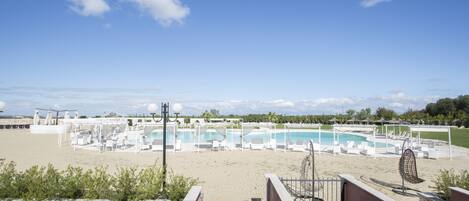 A pool area with multiple pools, lounge chairs, and umbrellas, surrounded by a stone wall and a clear sky.