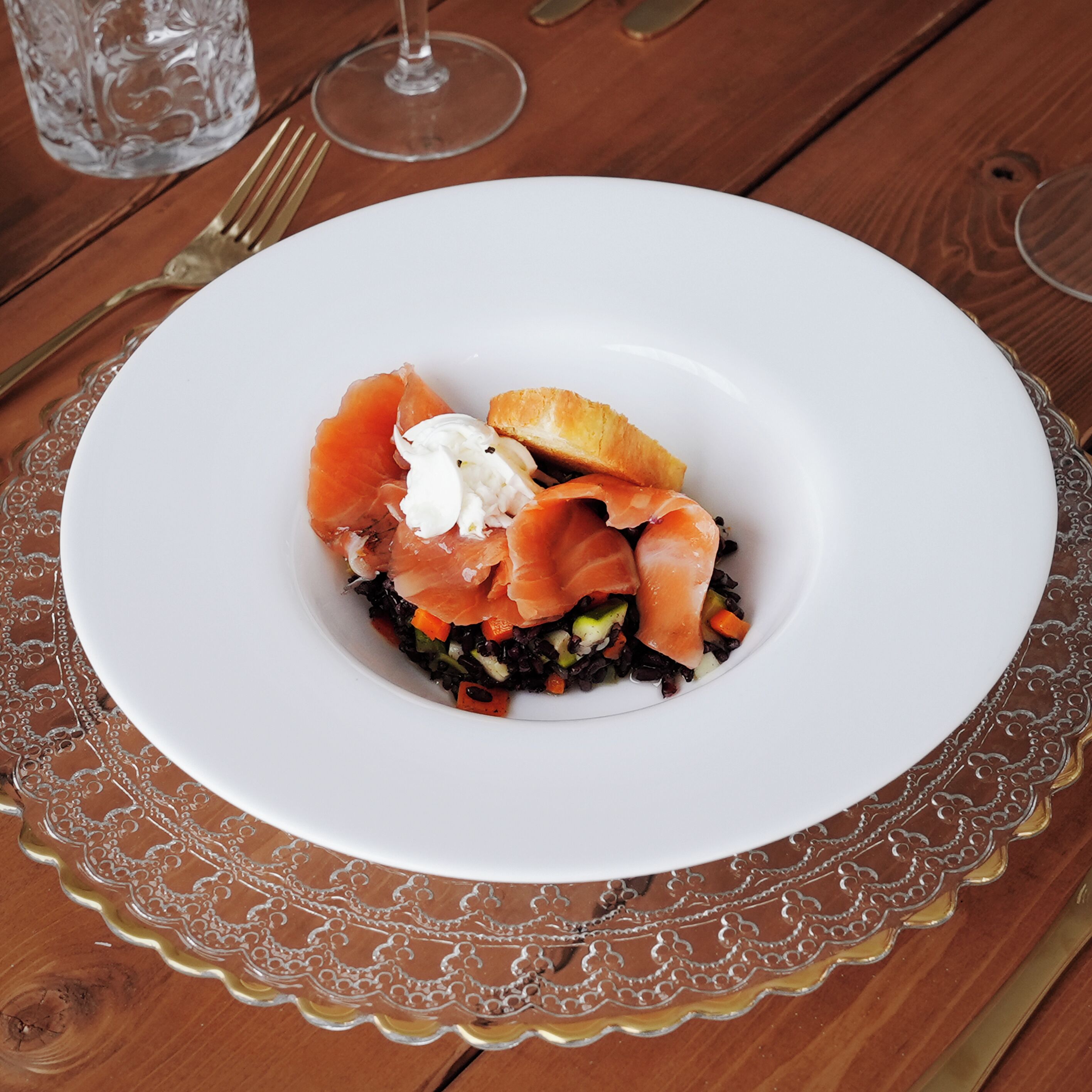 A white plate with smoked salmon, cream, and vegetables on a wooden table.