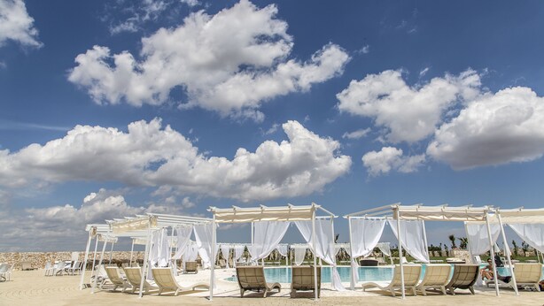 Resort à beira-mar com toldos brancos sobre áreas de estar e uma piscina.