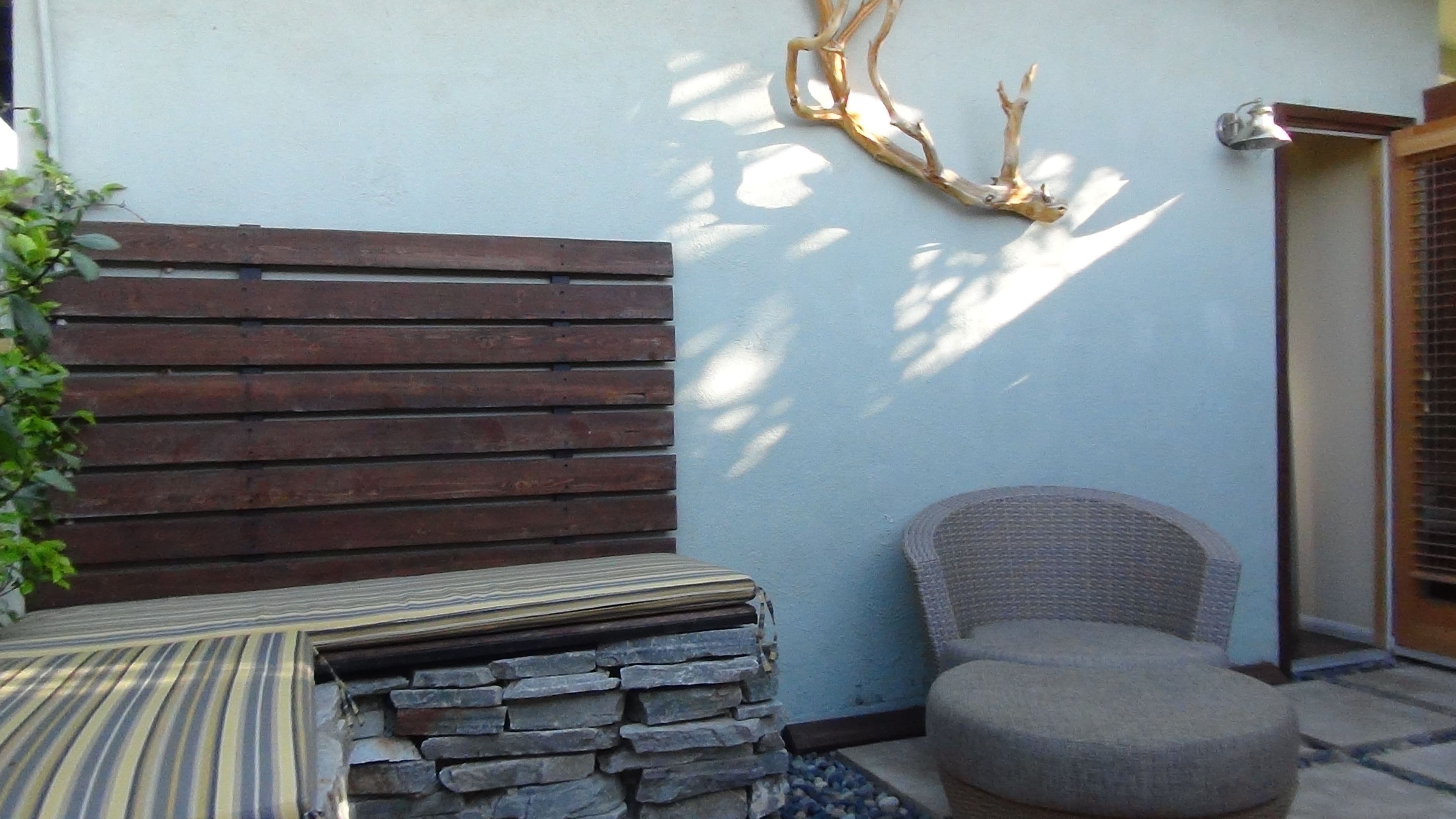 Un rincón con un banco de madera, una pared de piedra y una silla de mimbre.