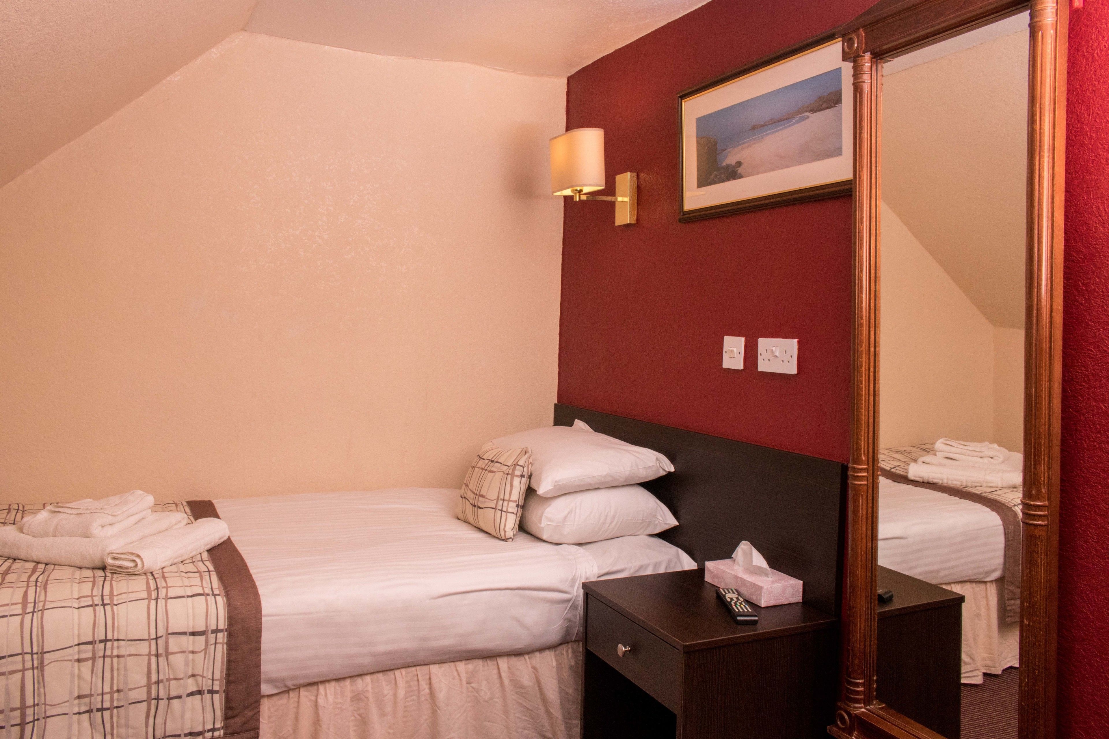 A hotel room with two beds, a bedside table with a lamp, a framed picture on the wall, and a mirror.