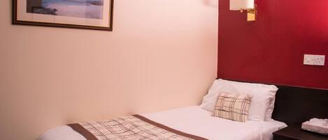 Una cama bien hecha con una manta escocesa, una mesita de noche con un control remoto y una lámpara de pared.