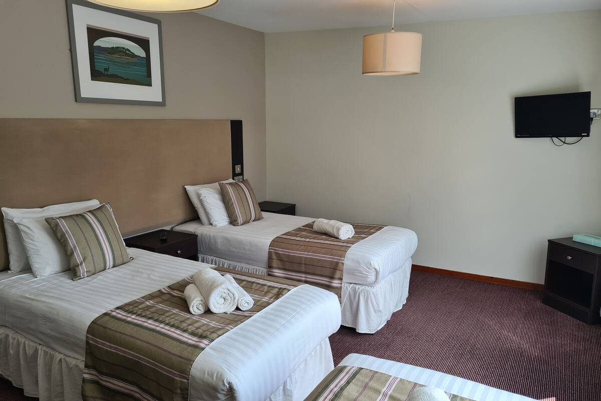 A hotel room with two beds, a TV, and a framed picture on the wall.