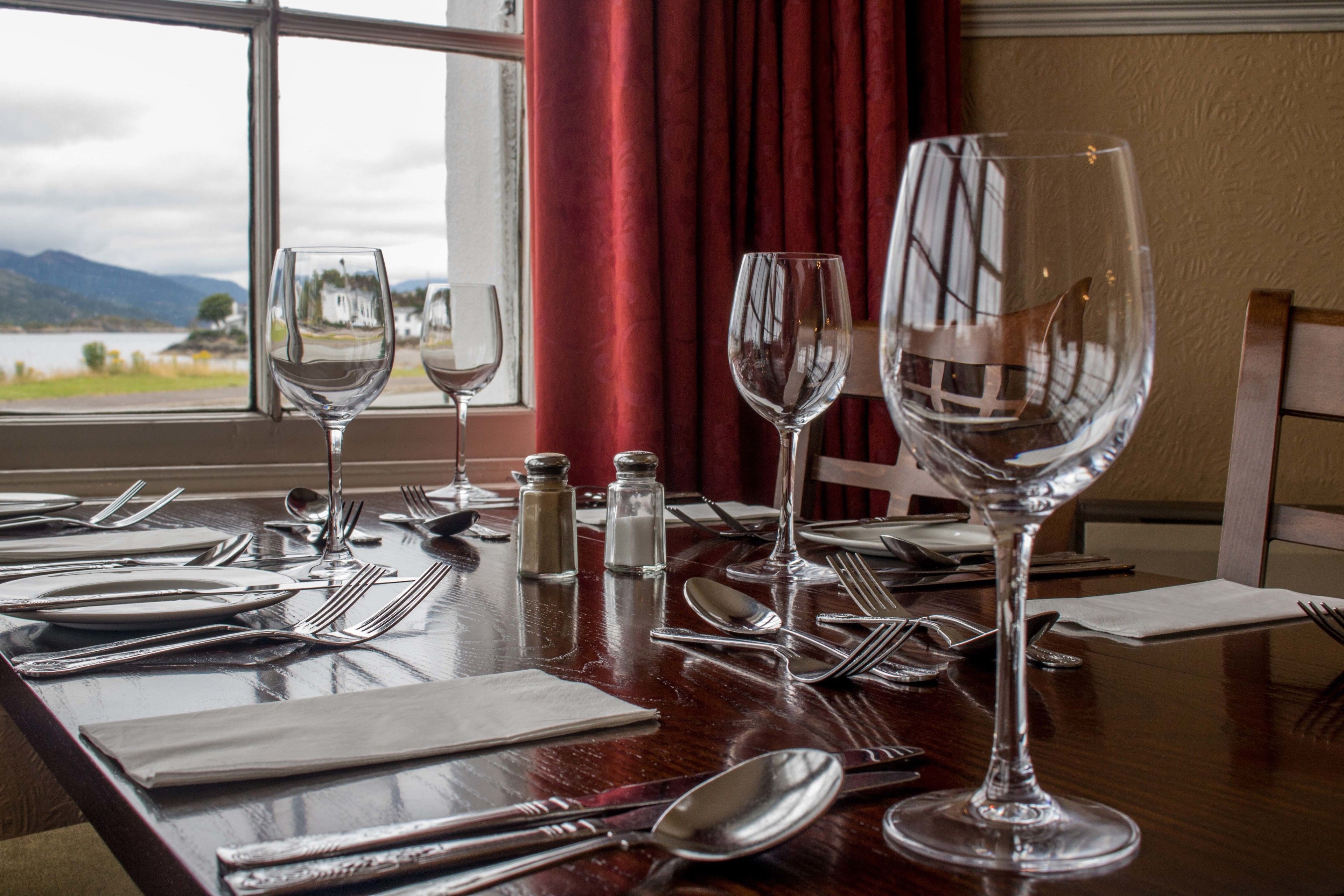 Une table à manger dressée pour un repas, avec des verres à vin, des couverts et des salières et poivrières.
