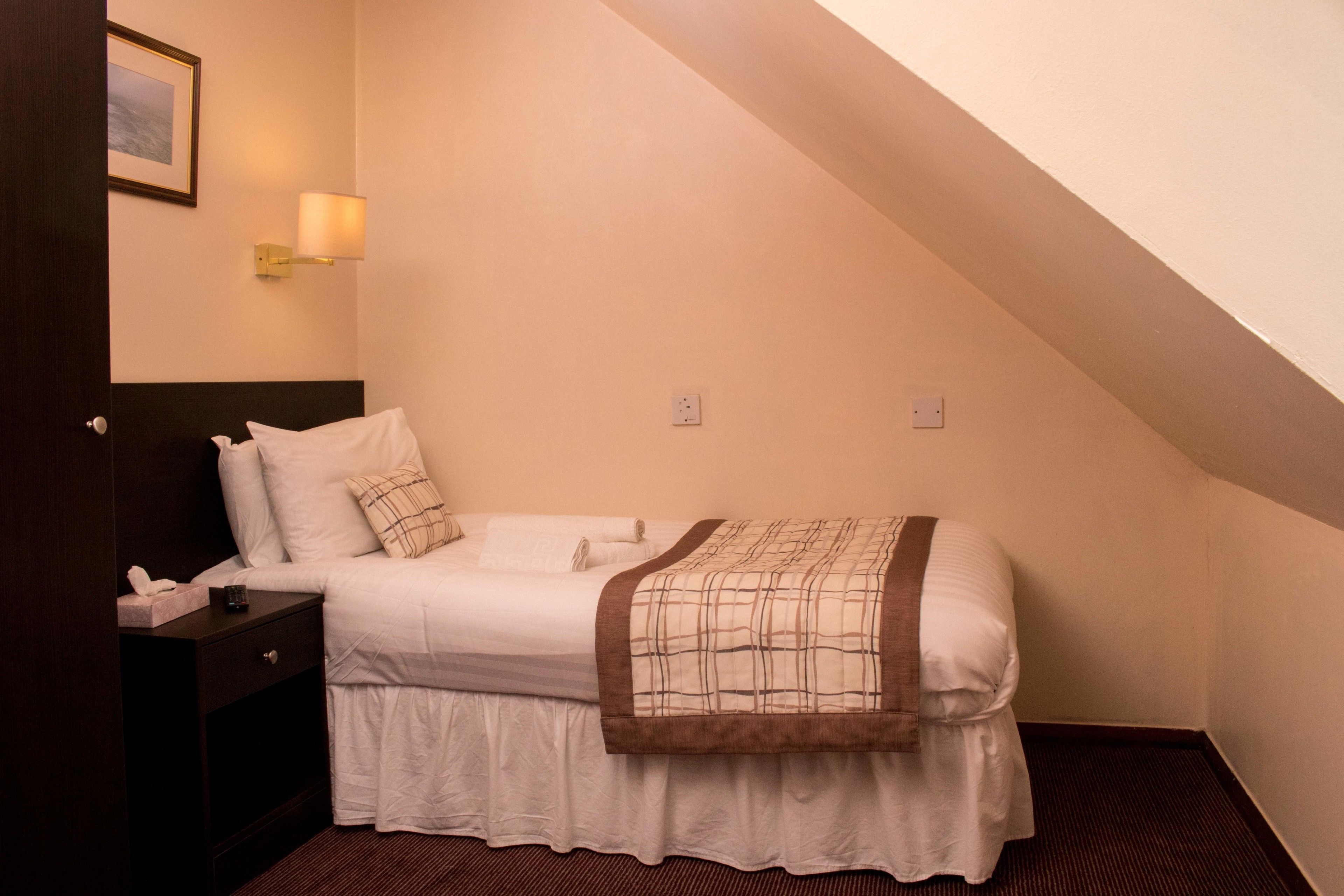 Una habitación de hotel con una cama individual, una mesita de noche, una lámpara y un cuadro en la pared.