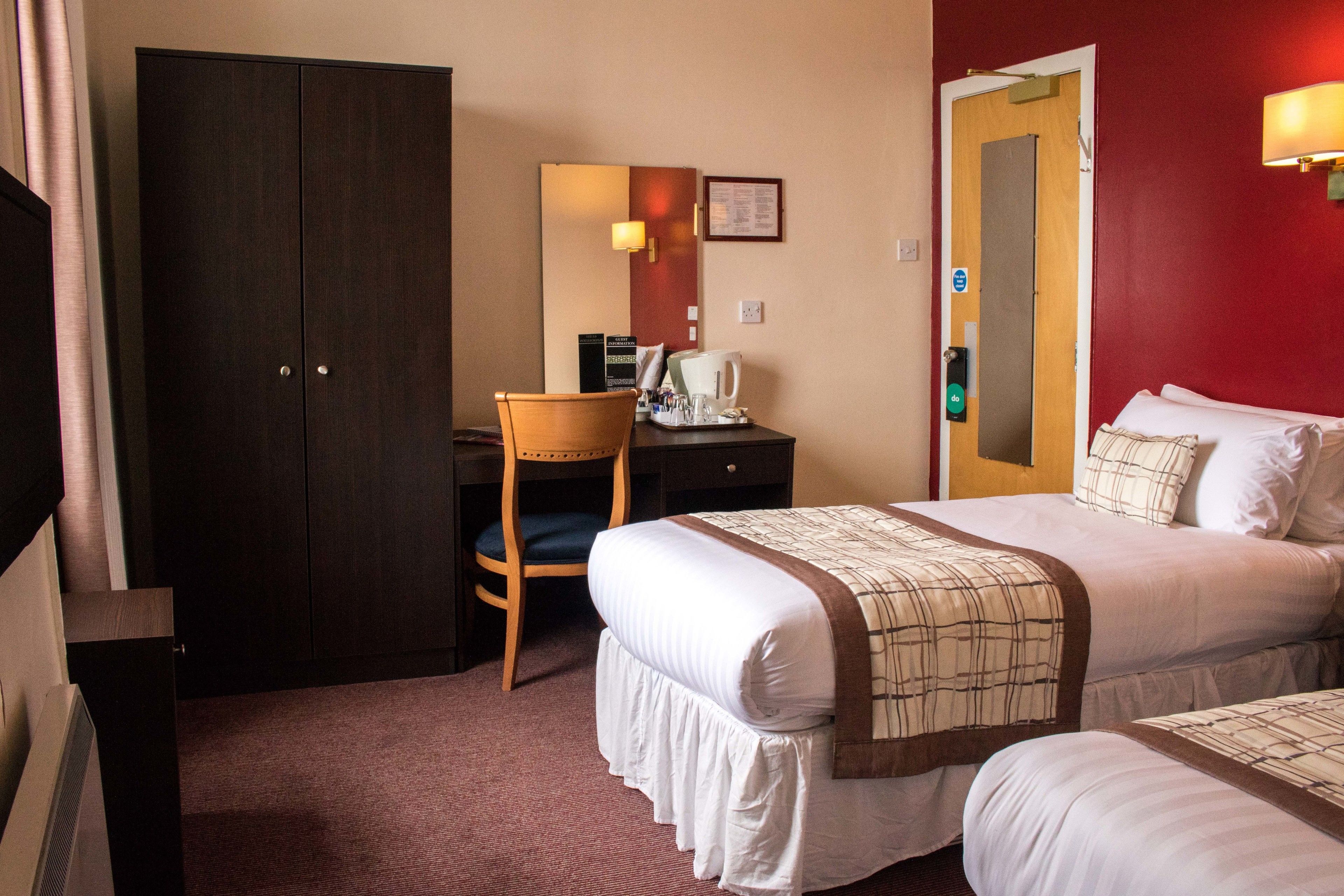 Una habitación de hotel con cama, escritorio, silla, armario y puerta.