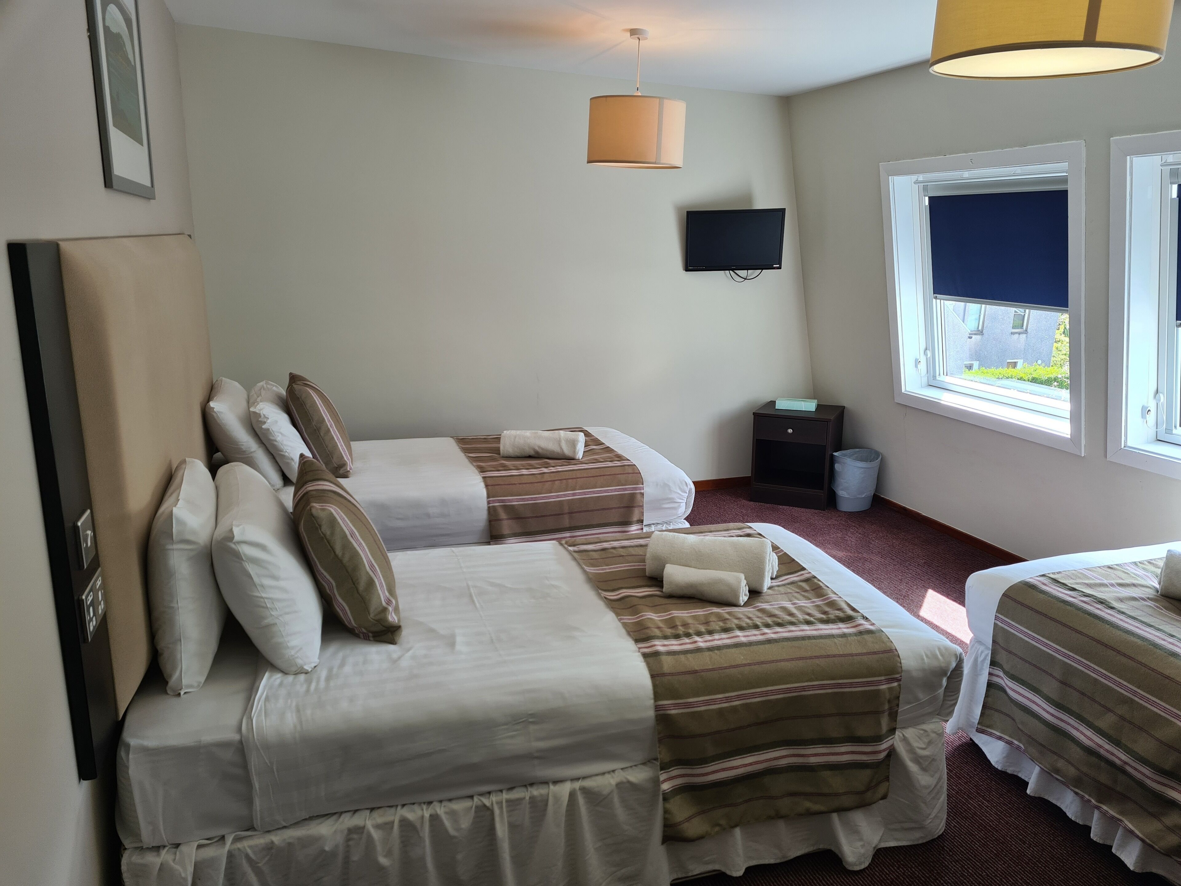 A hotel room with two beds, a TV, a window with a view, and a lamp.