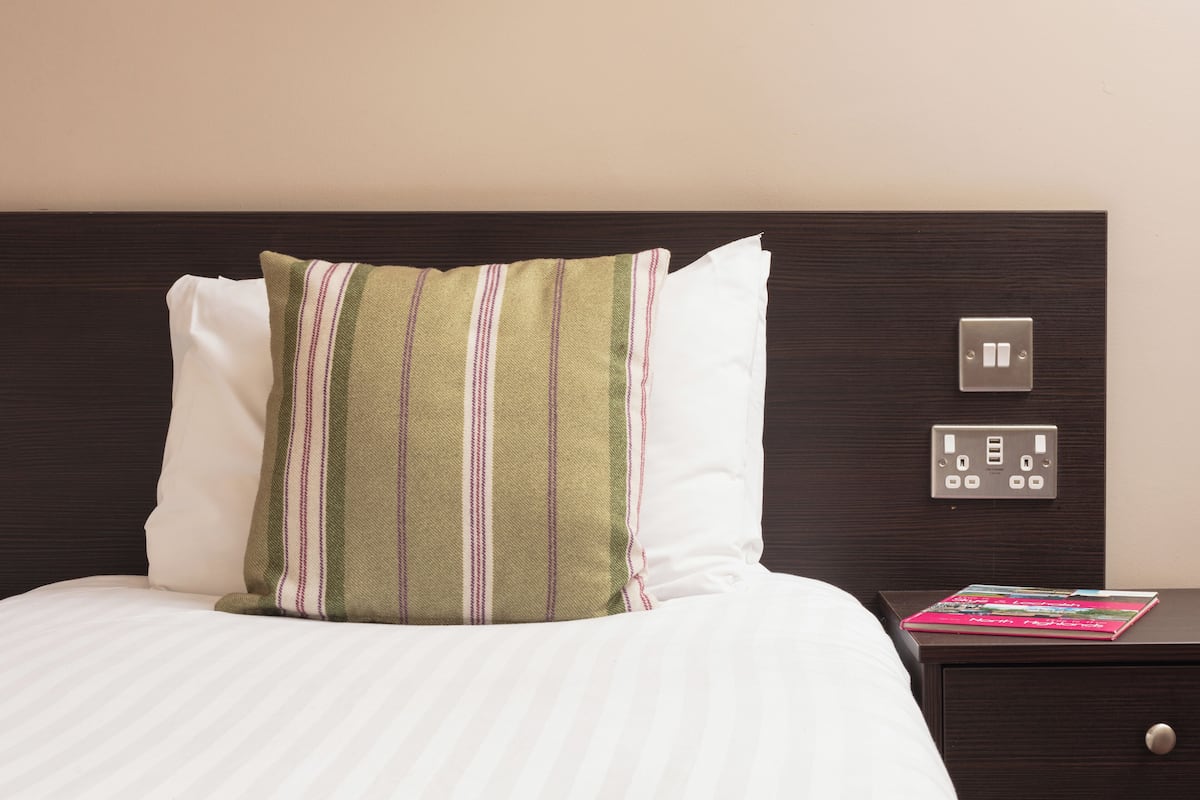A neatly made bed with striped pillows and a book on a bedside table.