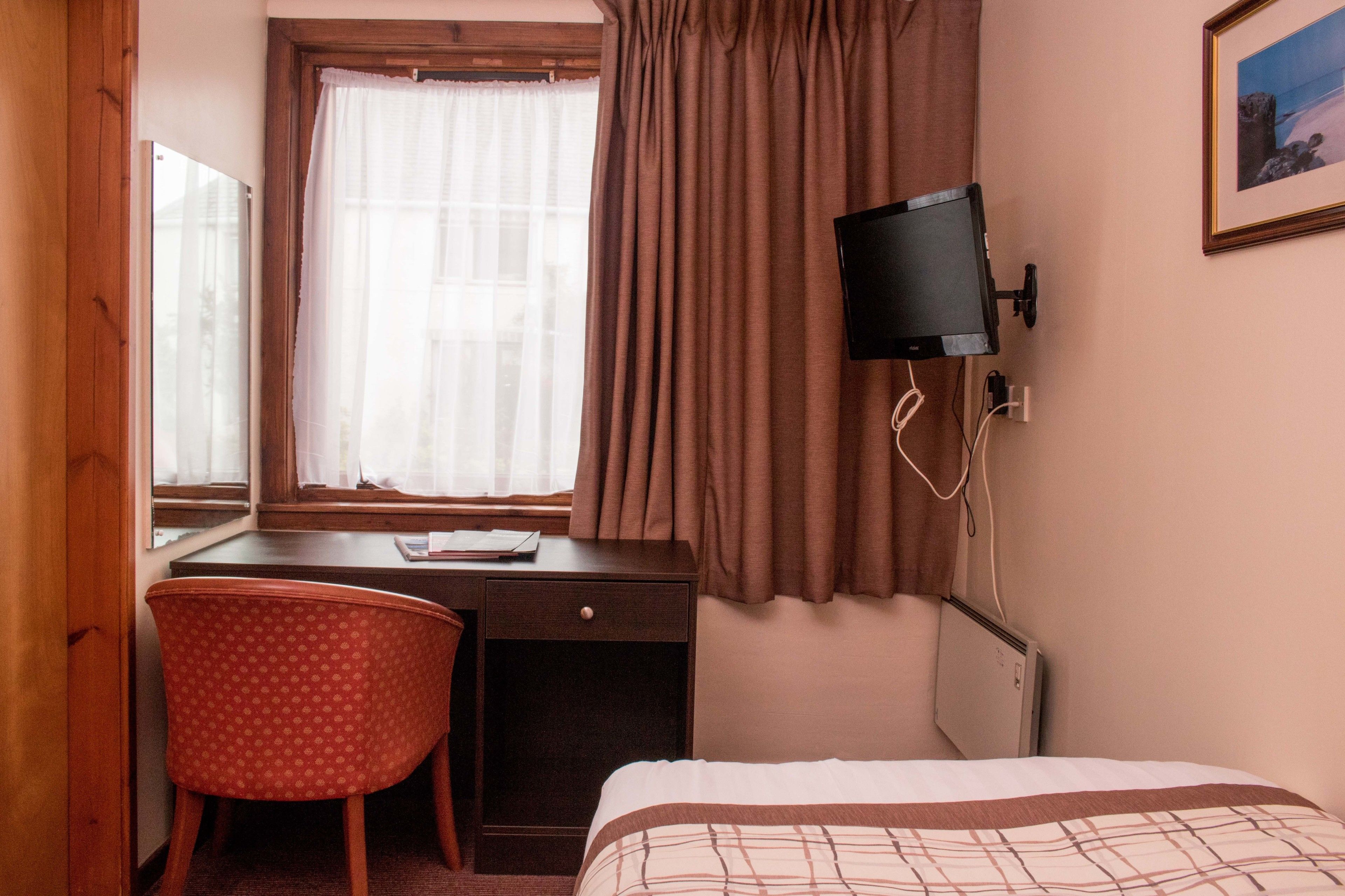 Habitación de hotel con cama, escritorio con silla, televisor y ventana con cortinas.
