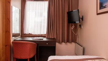 Habitación de hotel con cama, escritorio con silla, televisor y ventana con cortinas.
