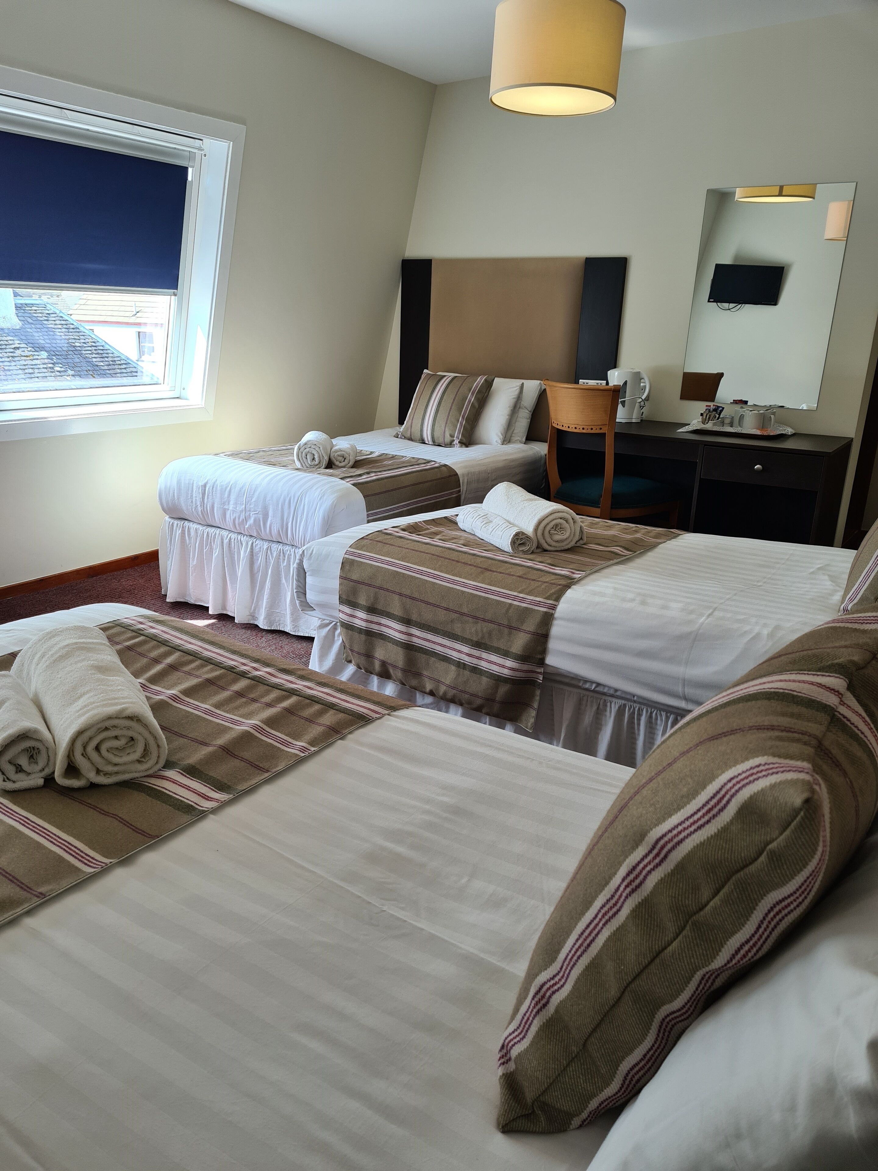 A hotel room with two beds, a desk, a chair, a coffee maker, and a large window.