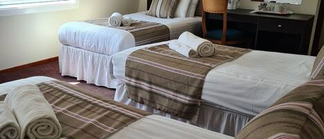A hotel room with two beds, a desk, a chair, a coffee maker, and a large window.