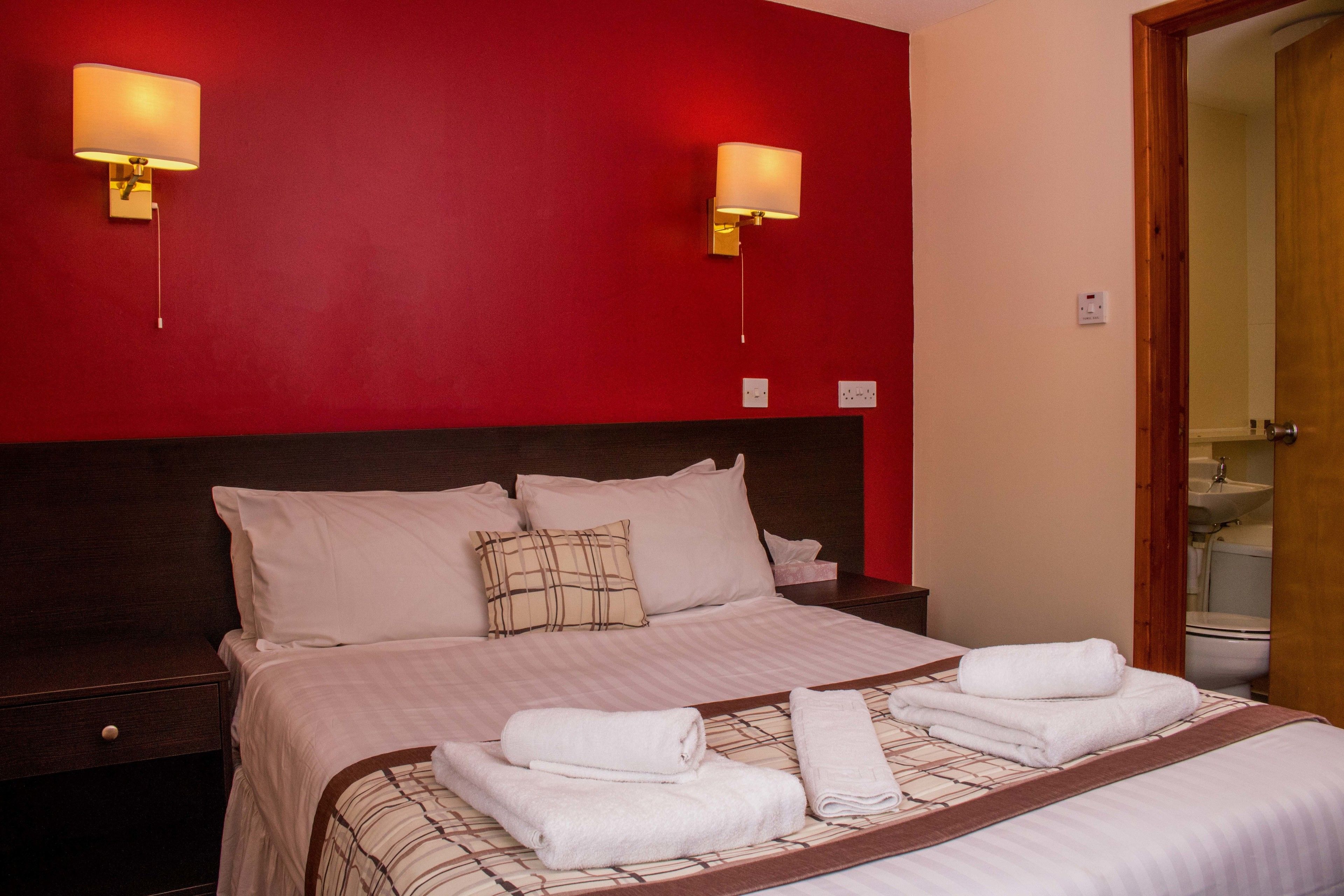 Habitación de hotel con una cama grande, dos lámparas de noche, una mesita de noche y un baño visible a través de una puerta abierta.