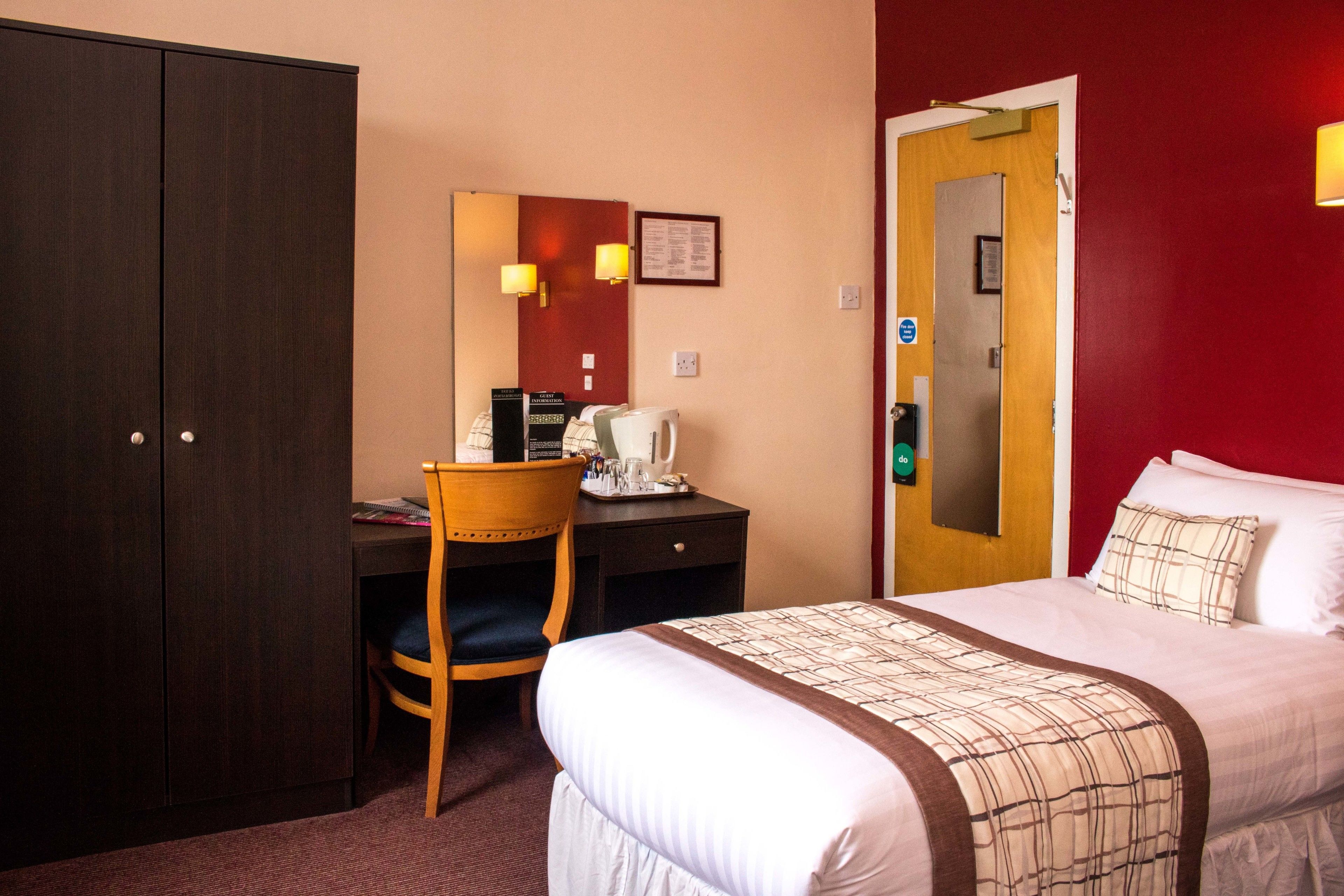 Habitación de hotel con cama, escritorio, silla, armario y puerta con espejo.