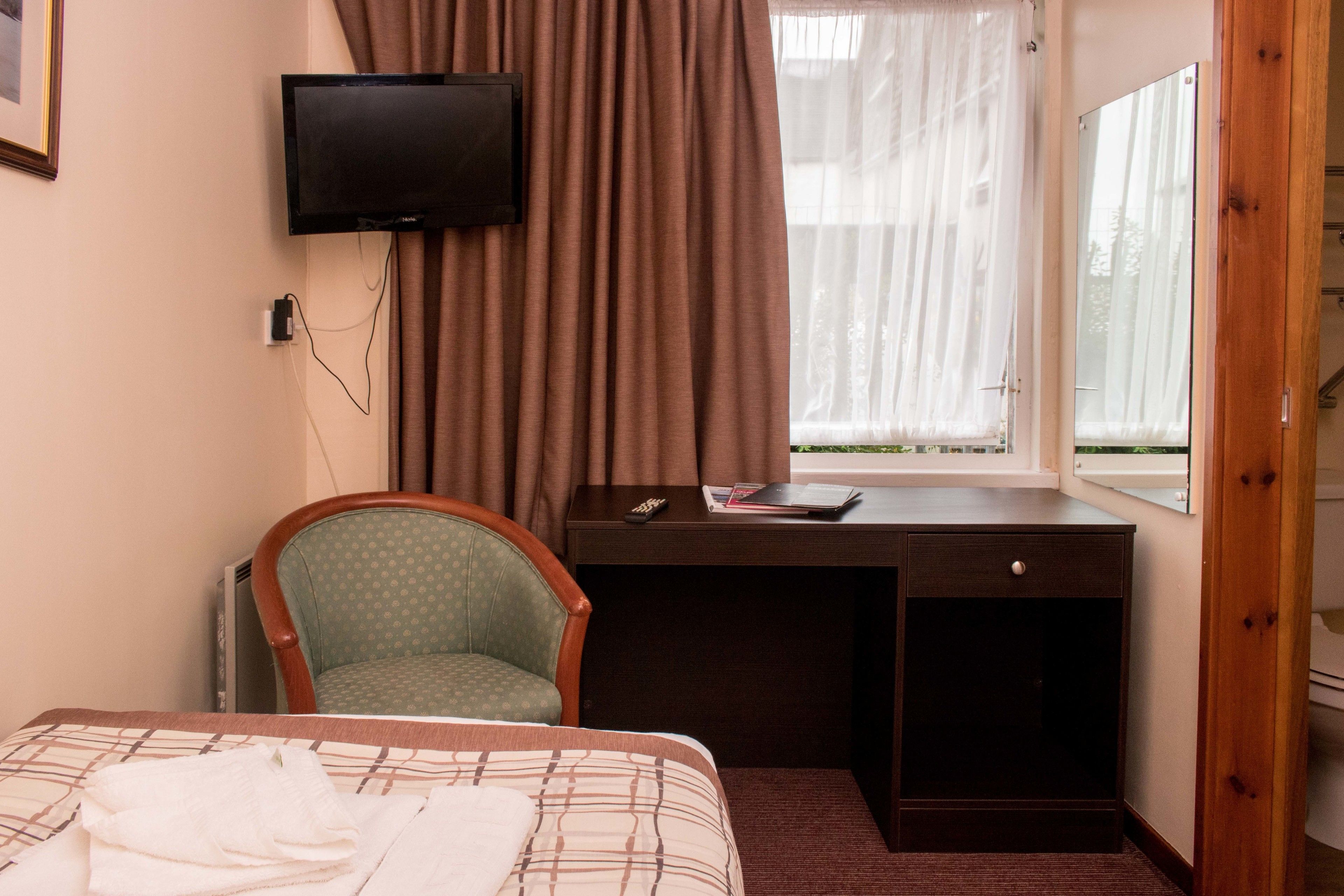 Een hotelkamer met een bed, een bureau, een stoel, een televisietoestel en een raam met gordijnen.
