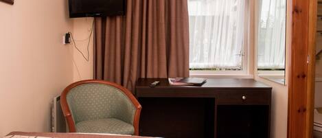 Een hotelkamer met een bed, een bureau, een stoel, een televisietoestel en een raam met gordijnen.