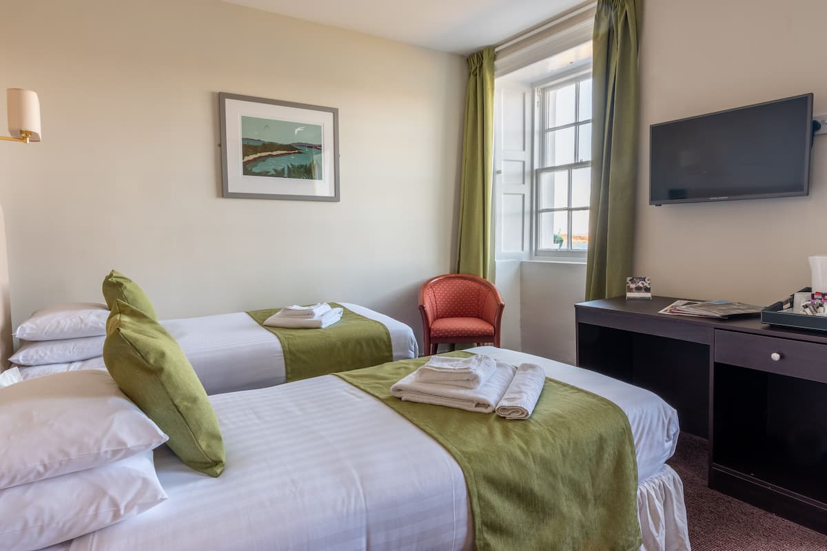 A hotel room with two beds, a desk, a chair, a TV, and a window with curtains.