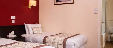 A hotel room with two beds, a red accent wall, a framed picture, and a bathroom visible through an open door.