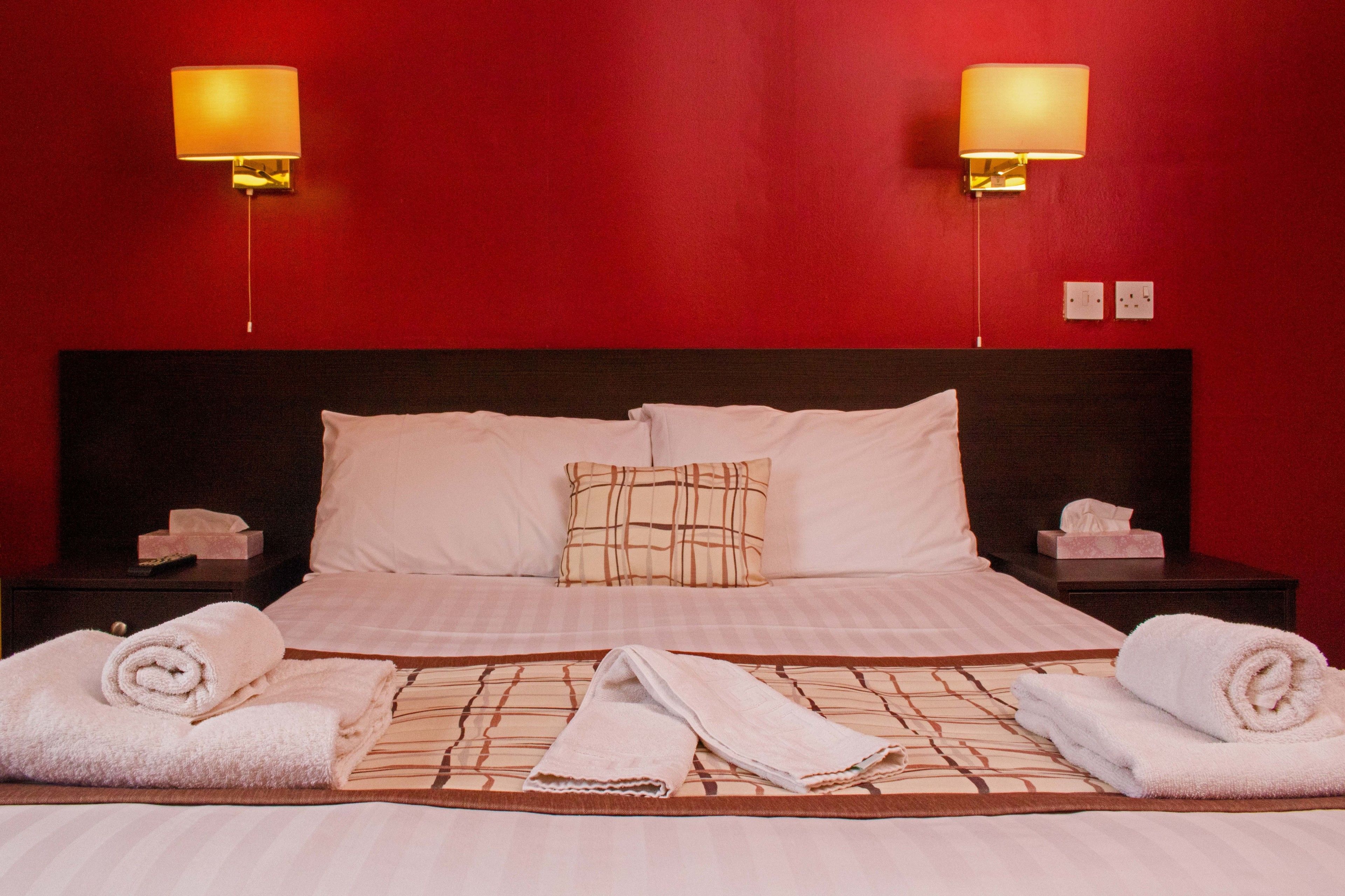 A neatly made bed with white linens, two bedside lamps, and a red wall.