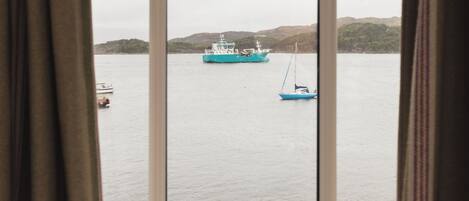 Vista a través de una ventana de una extensa masa de agua con un barco y un velero más pequeño.