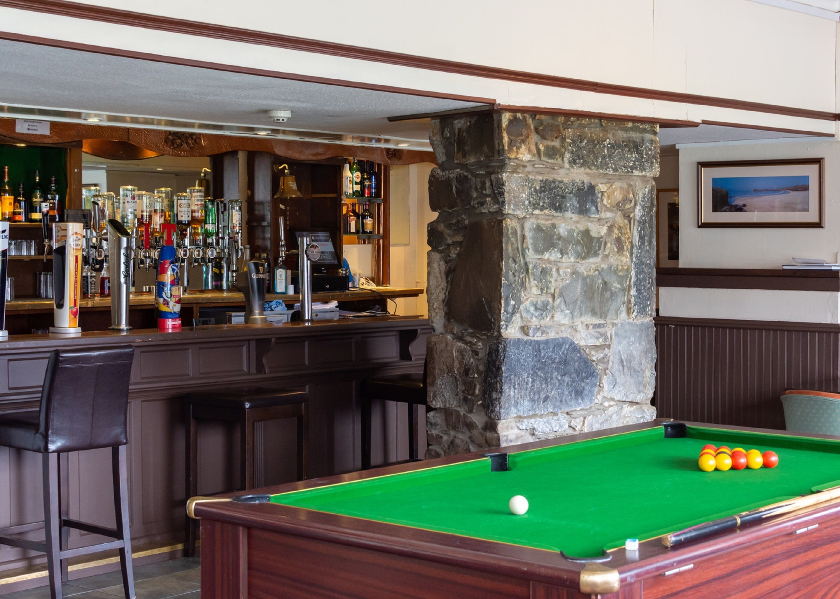 A bar area with a pool table, bar stools, and a stone pillar.