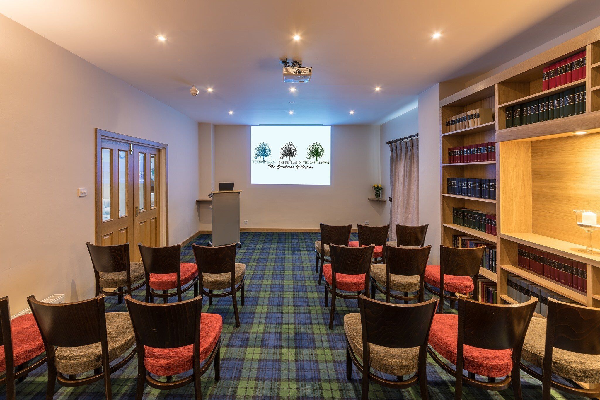 A conference room with a projector screen, rows of chairs, and a bookshelf.