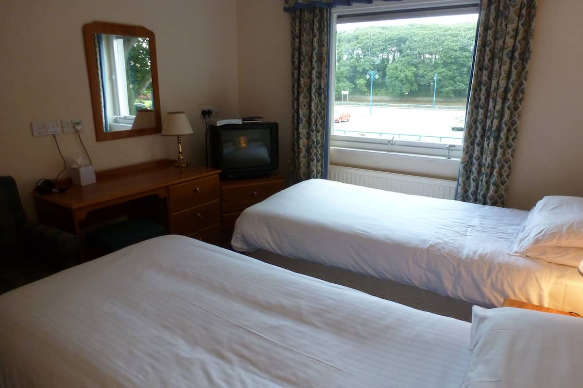 A hotel room with two beds, a desk with a lamp, a television, and a window with curtains.