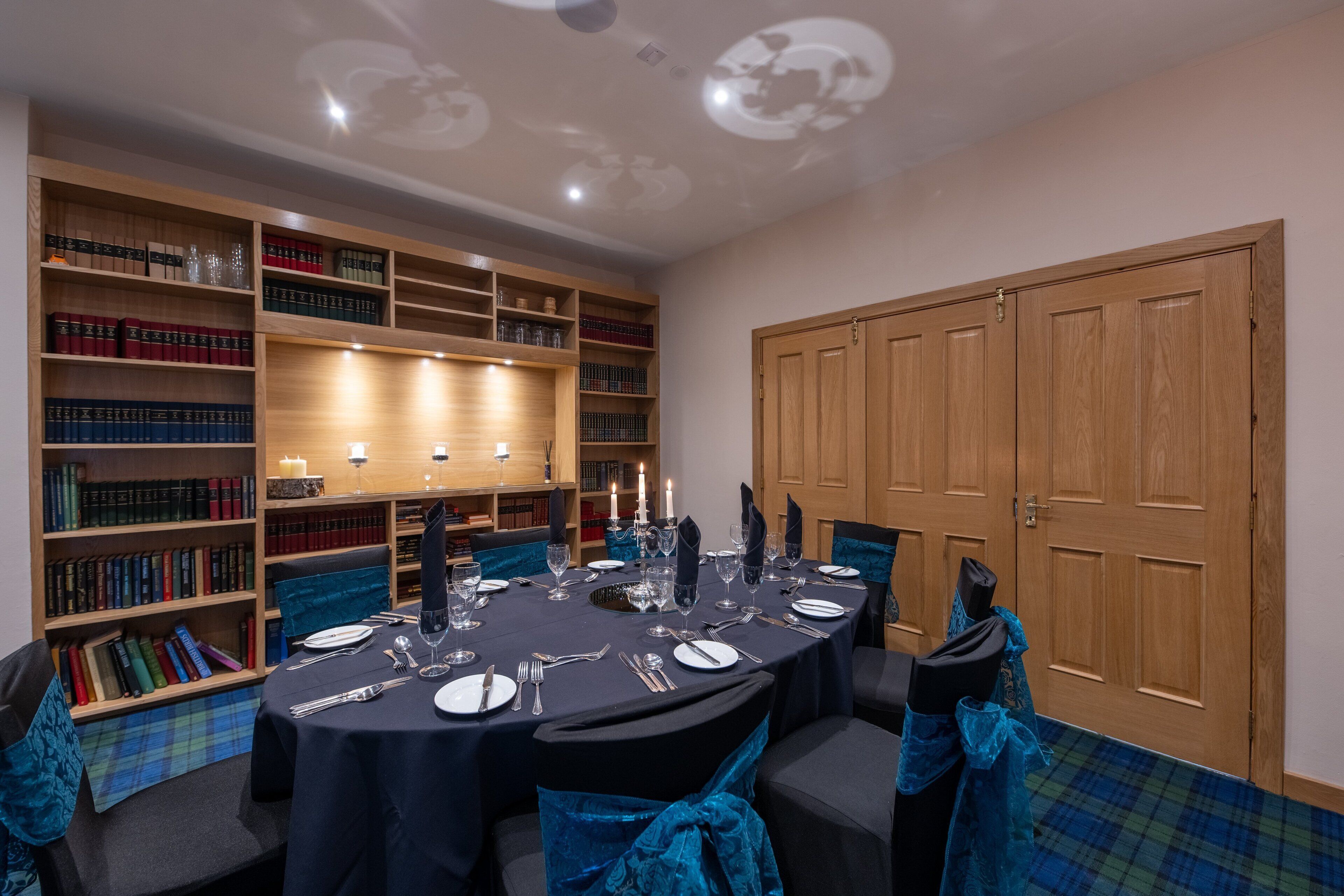 A conference room with a round table set for a meeting, surrounded by bookshelves filled with books, and a wooden door in the background.