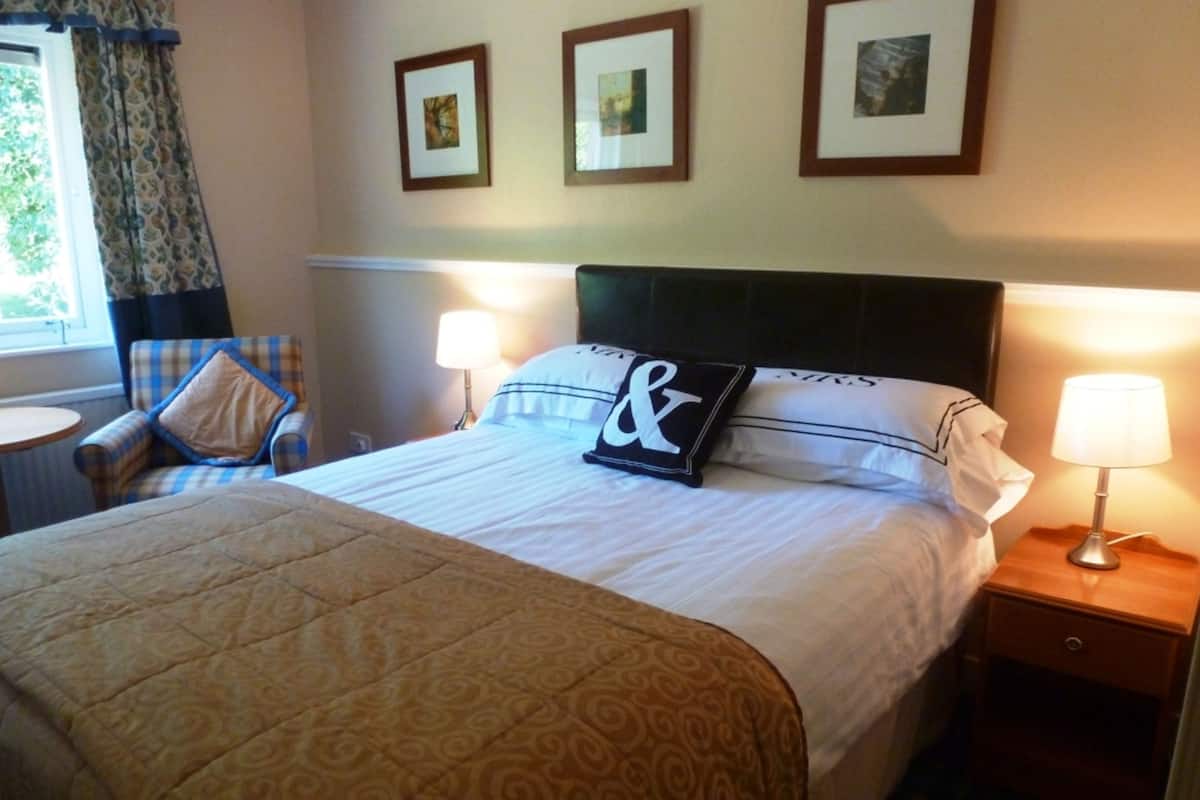 A hotel room with a large bed, two bedside lamps, a chair, and three framed pictures on the wall.