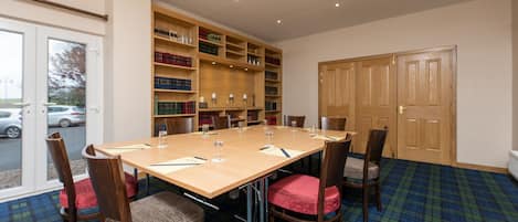 Un salón de conferencias con una mesa larga, sillas, una estantería y una puerta.