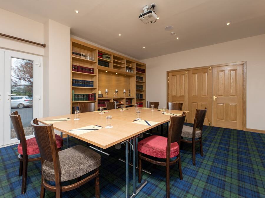 A conference room with a long table, chairs, a bookshelf, and a door.